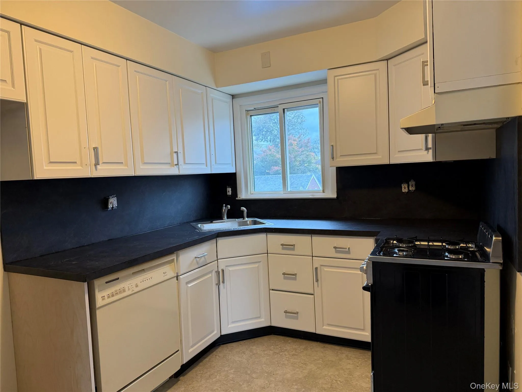 Kitchen with dark countertops, range with gas stovetop, white cabinets, and dishwasher Kitchen with dark countertops, range with gas stovetop, white cabinets, and dishwasher