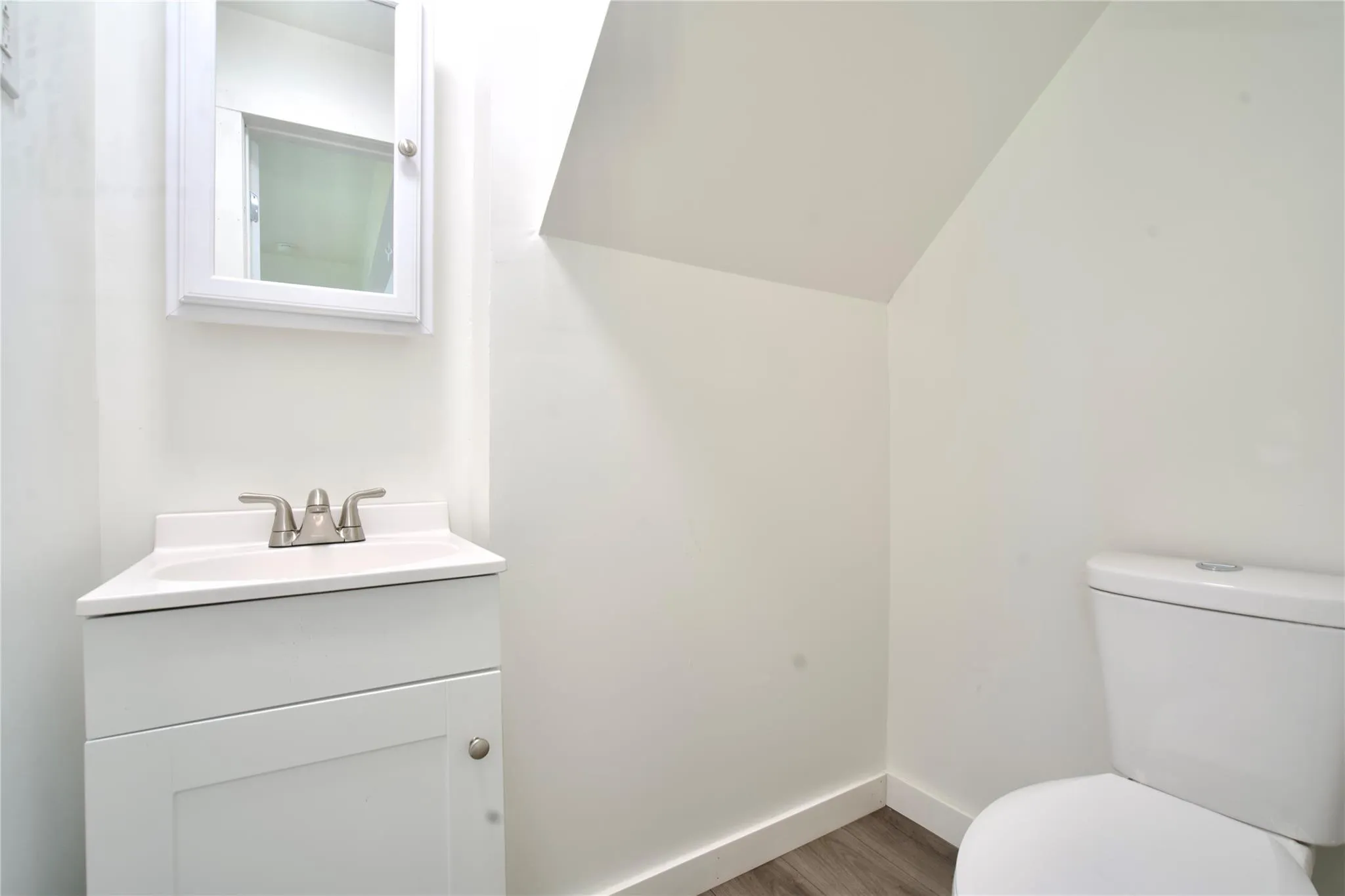 Half bathroom featuring vanity, lofted ceiling, and wood finished floors Half bathroom featuring vanity, lofted ceiling, and wood finished floors