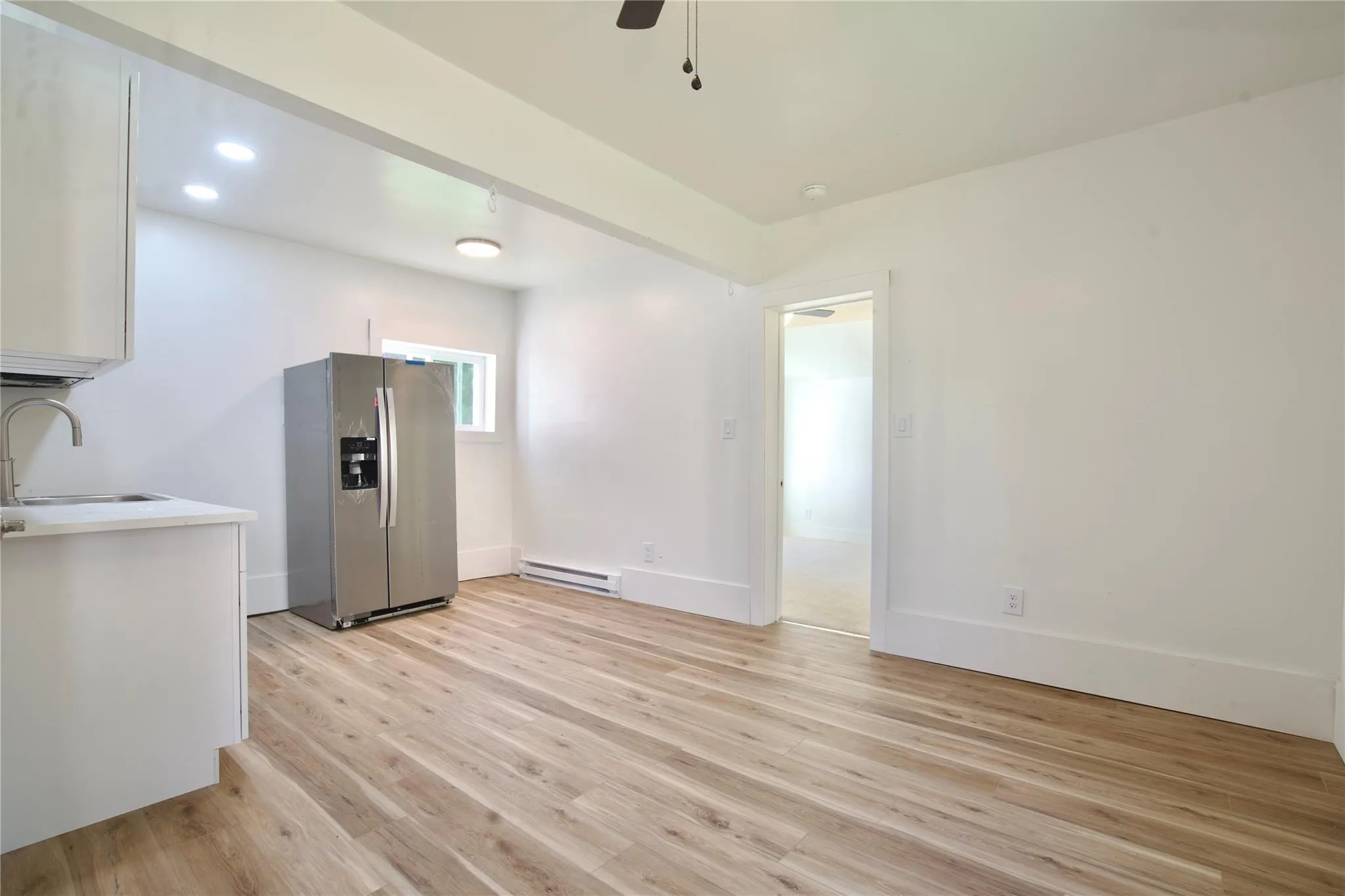 EIK featuring stainless steel fridge, light wood finished floors, white cabinetry, ceiling fan, and a baseboard heating unit EIK featuring stainless steel fridge, light wood finished floors, white cabinetry, ceiling fan, and a baseboard heating unit