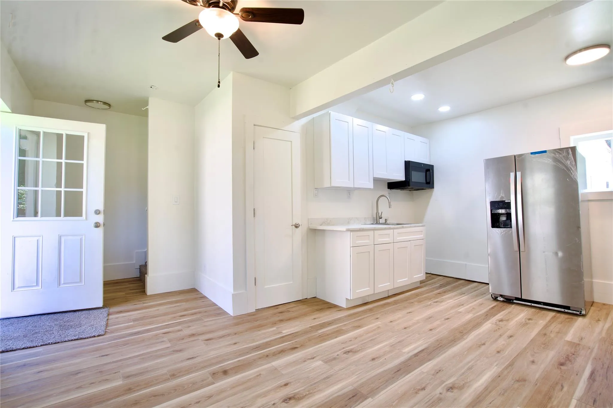 Kitchen with stainless steel refrigerator with ice dispenser, light countertops, light wood finished floors, white cabinetry, and black microwave Kitchen with stainless steel refrigerator with ice dispenser, light countertops, light wood finished floors, white cabinetry, and black microwave