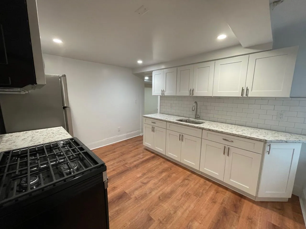 Kitchen with black gas stove, light wood-style flooring, decorative backsplash, light stone countertops, and white cabinets Kitchen with black gas stove, light wood-style flooring, decorative backsplash, light stone countertops, and white cabinets