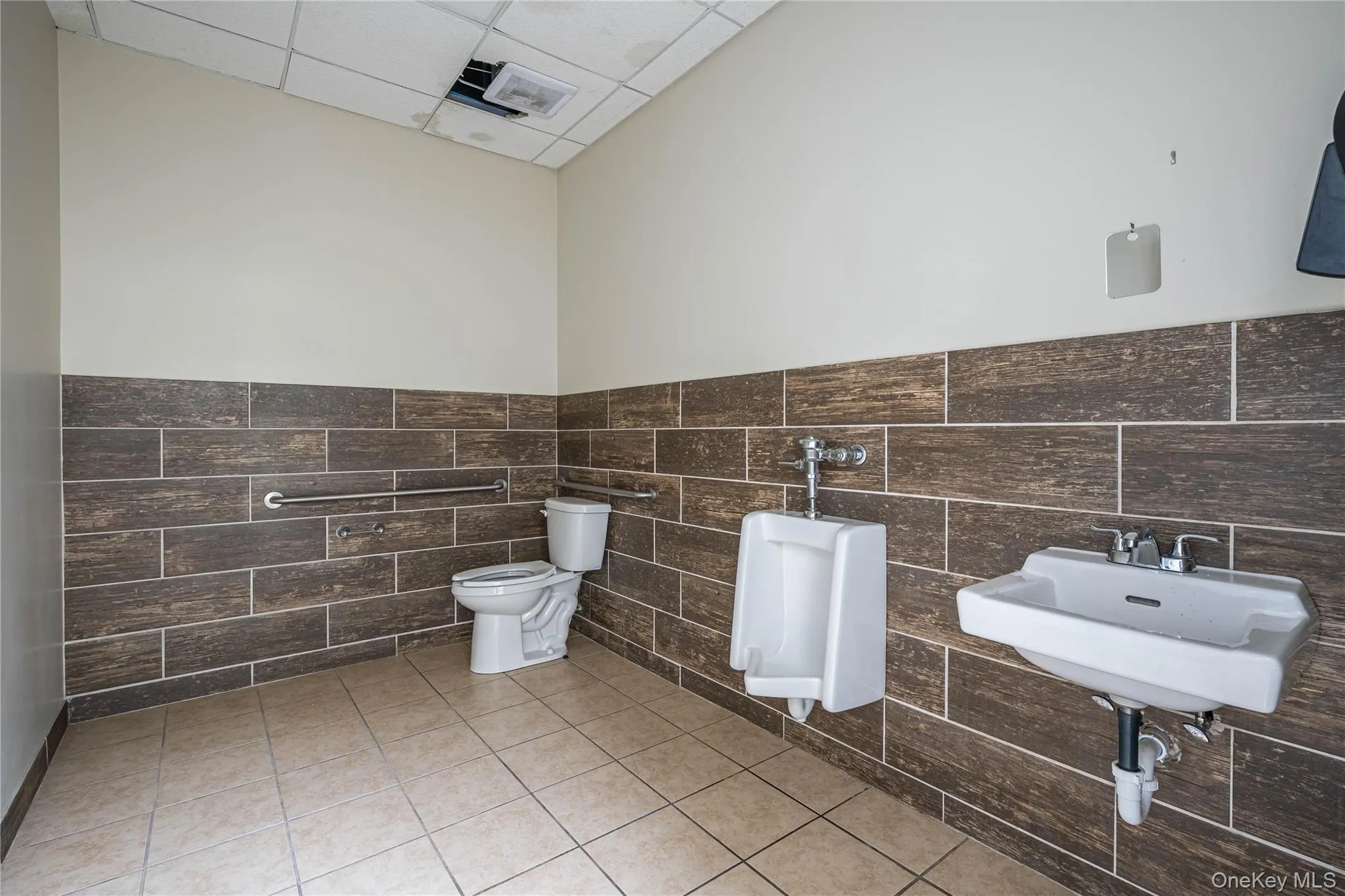 Bathroom with light tile patterned floors, tile walls, a paneled ceiling, and a wainscoted wall Bathroom with light tile patterned floors, tile walls, a paneled ceiling, and a wainscoted wall