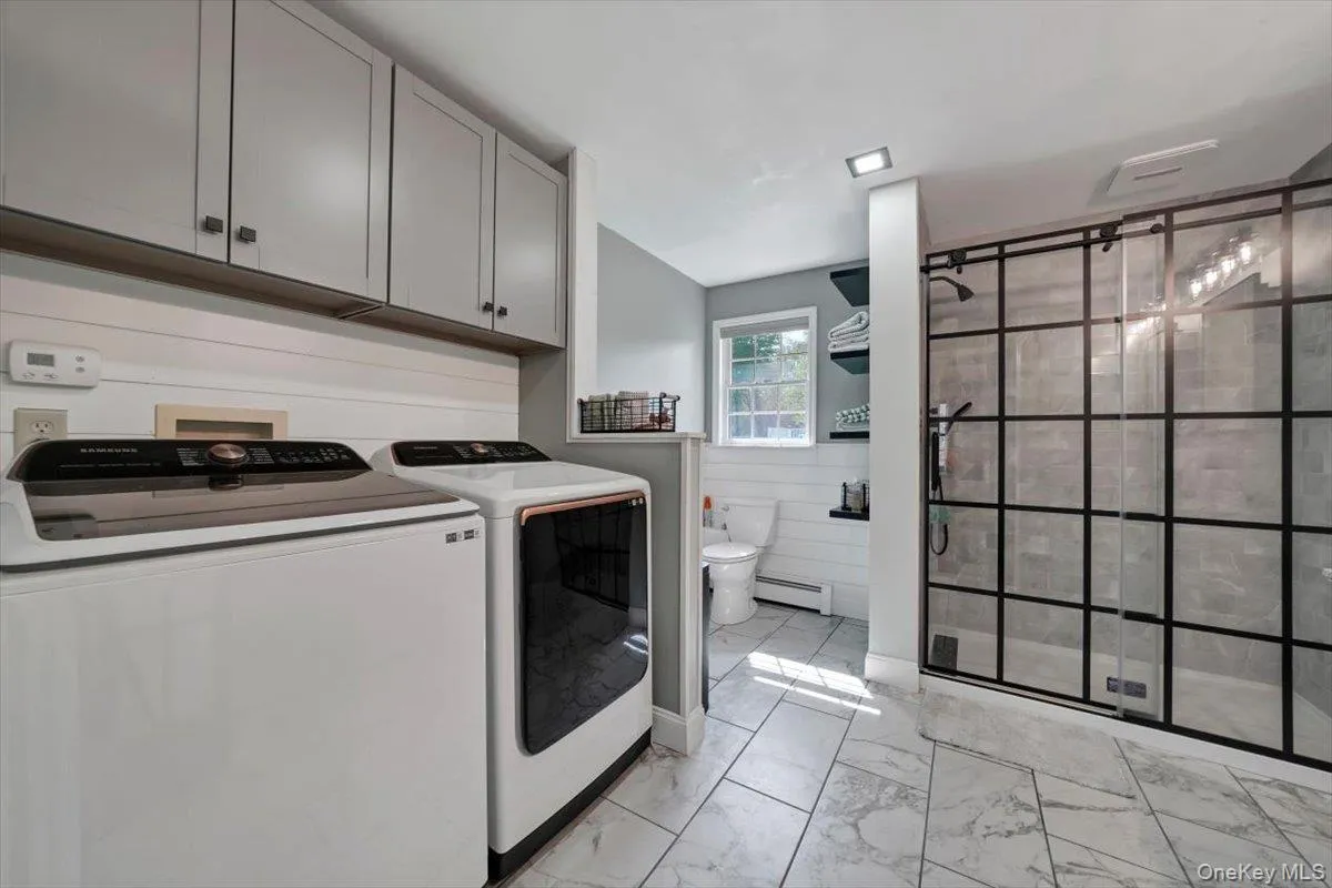 Laundry room with cabinet space, washer and dryer, light marble finish flooring, wainscoting, and a baseboard heating unit Laundry room with cabinet space, washer and dryer, light marble finish flooring, wainscoting, and a baseboard heating unit
