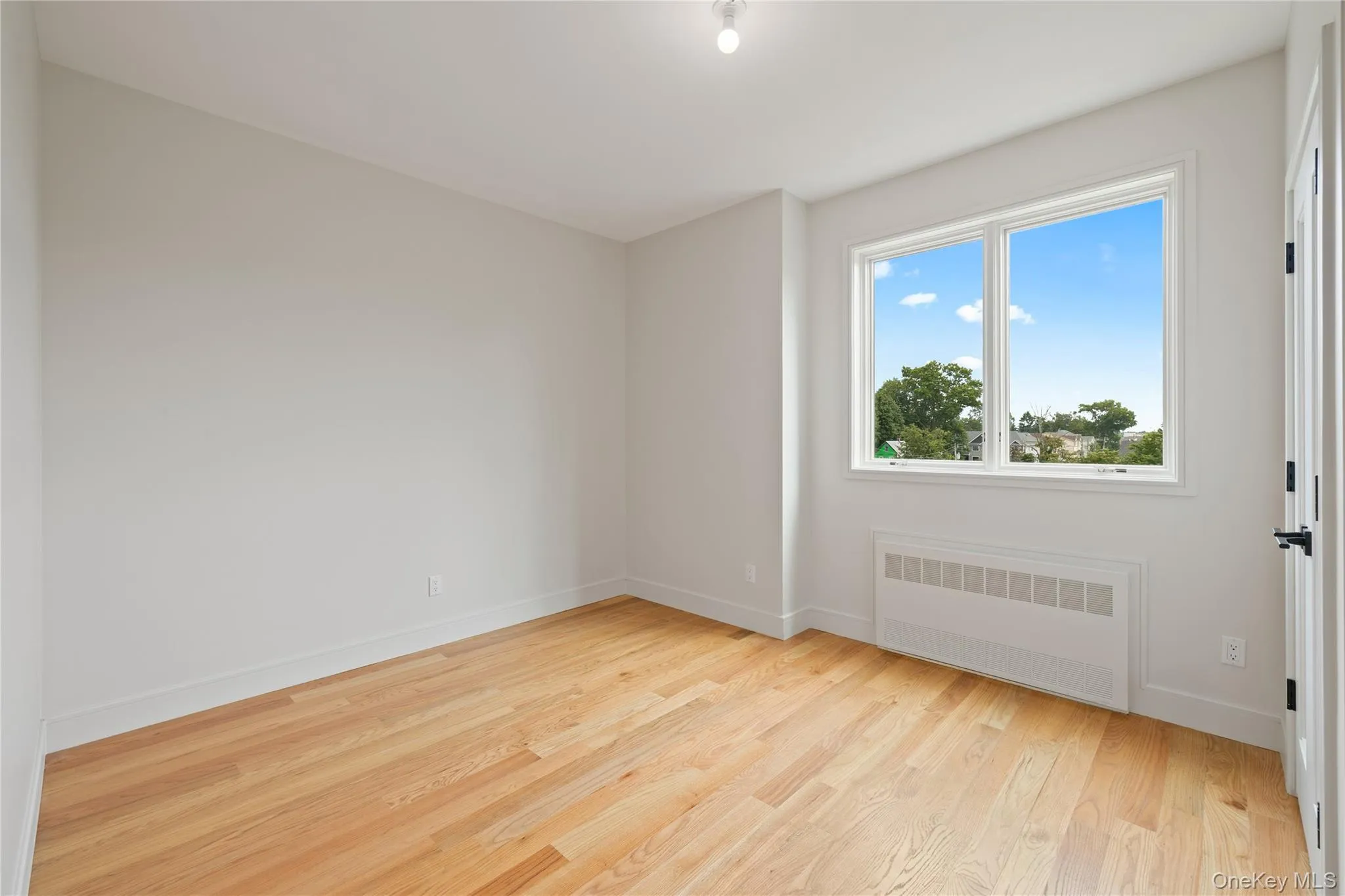 Unfurnished room with radiator heating unit and light wood finished floors Unfurnished room with radiator heating unit and light wood finished floors