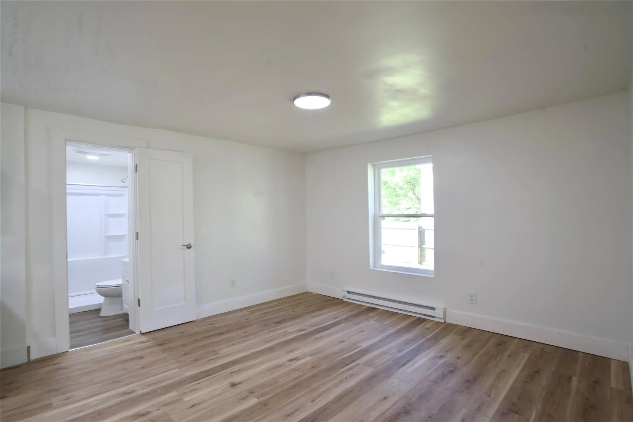 Unfurnished bedroom with a baseboard heating unit, light wood finished floors, and ensuite bath Unfurnished bedroom with a baseboard heating unit, light wood finished floors, and ensuite bath