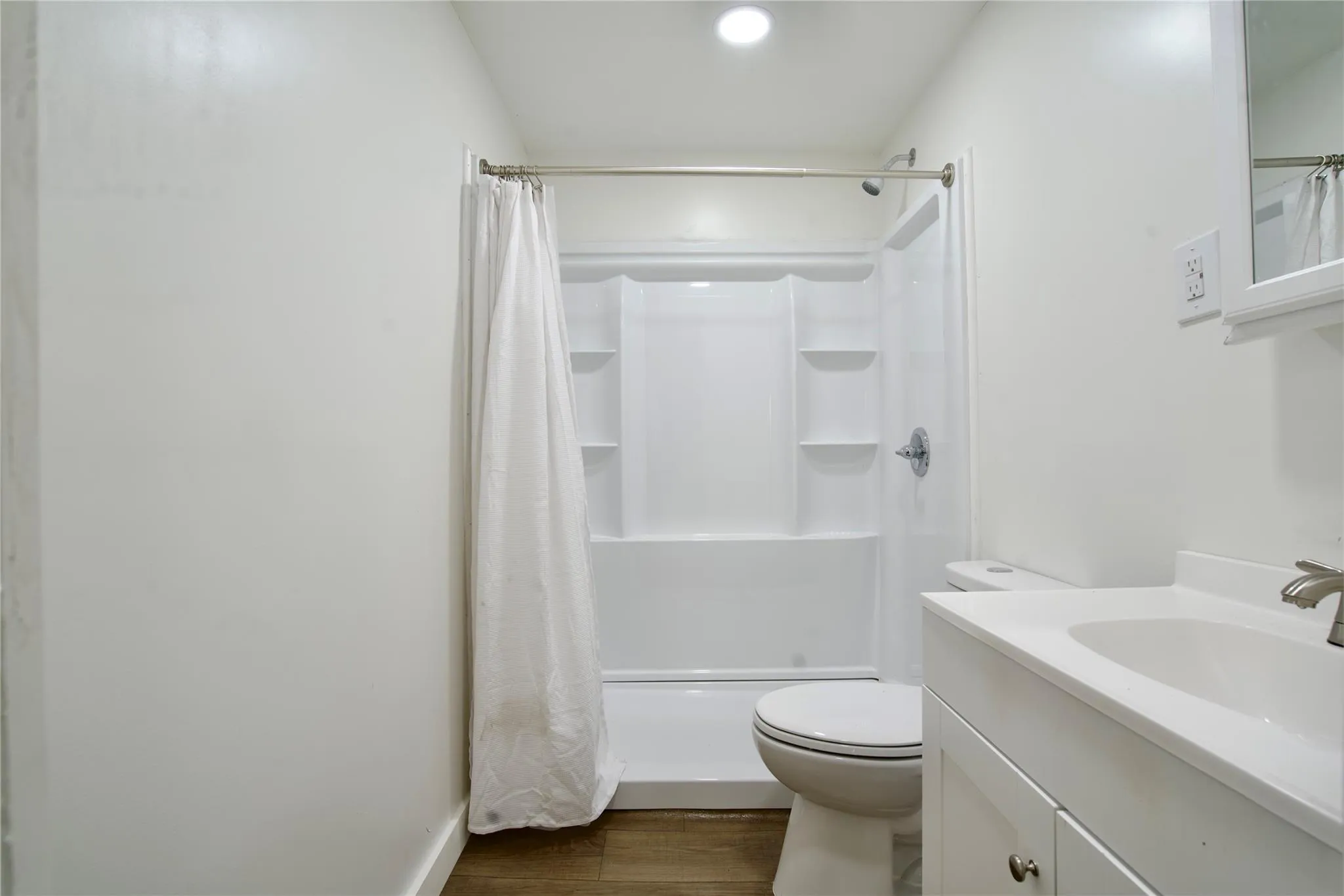 Full bathroom with wood finished floors, vanity, and shower / bathtub combination with curtain Full bathroom with wood finished floors, vanity, and shower / bathtub combination with curtain