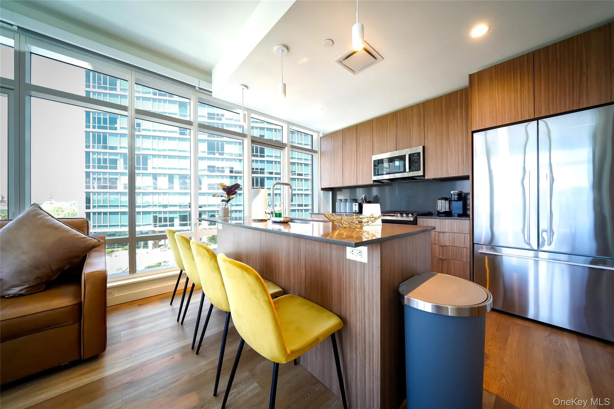 Kitchen with appliances with stainless steel finishes, healthy amount of natural light, brown cabinetry, a center island with sink, and a wall of windows Kitchen with appliances with stainless steel finishes, healthy amount of natural light, brown cabinetry, a center island with sink, and a wall of windows