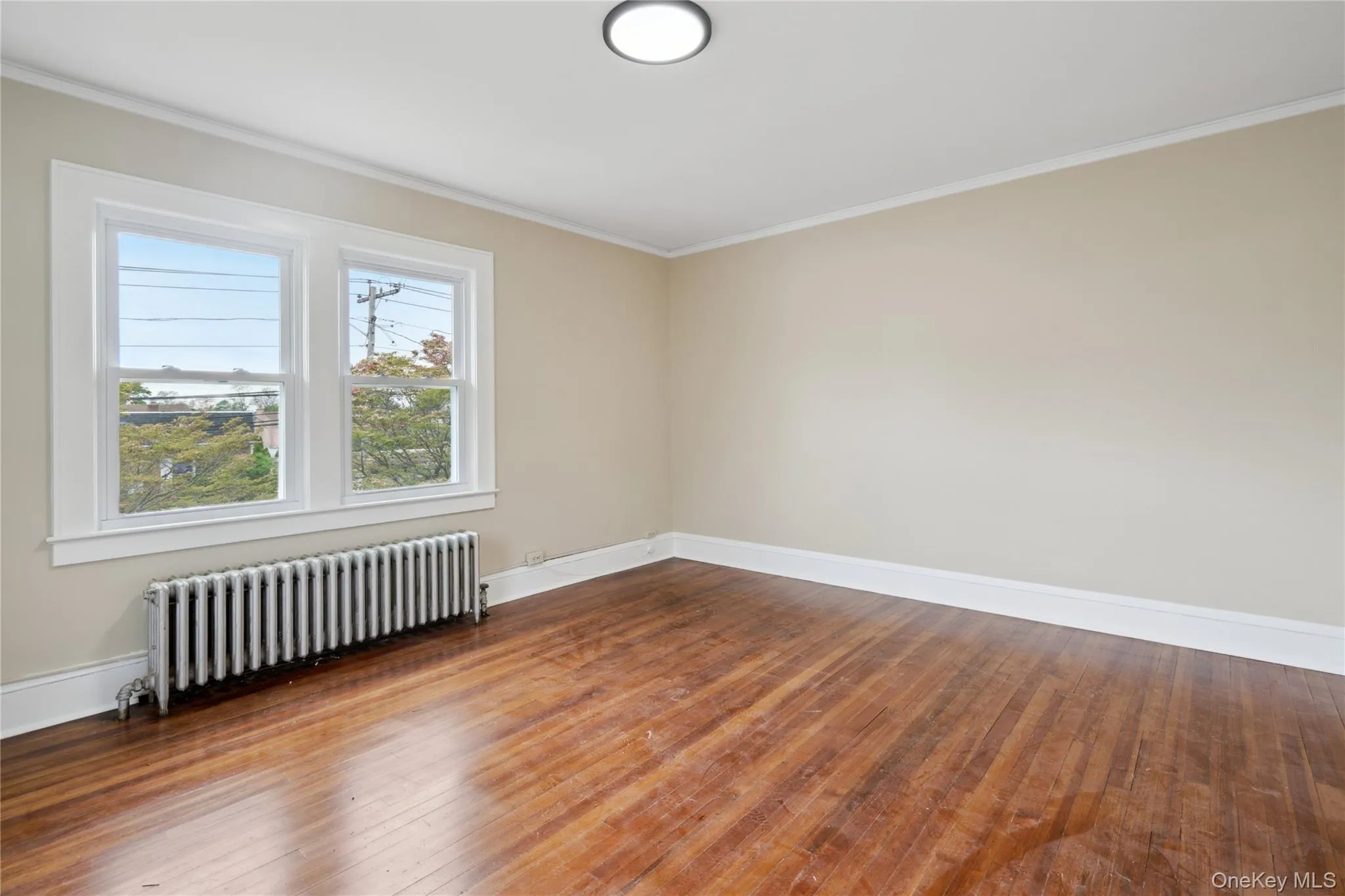 Spare room featuring radiator heating unit, crown molding, and wood-type flooring Spare room featuring radiator heating unit, crown molding, and wood-type flooring