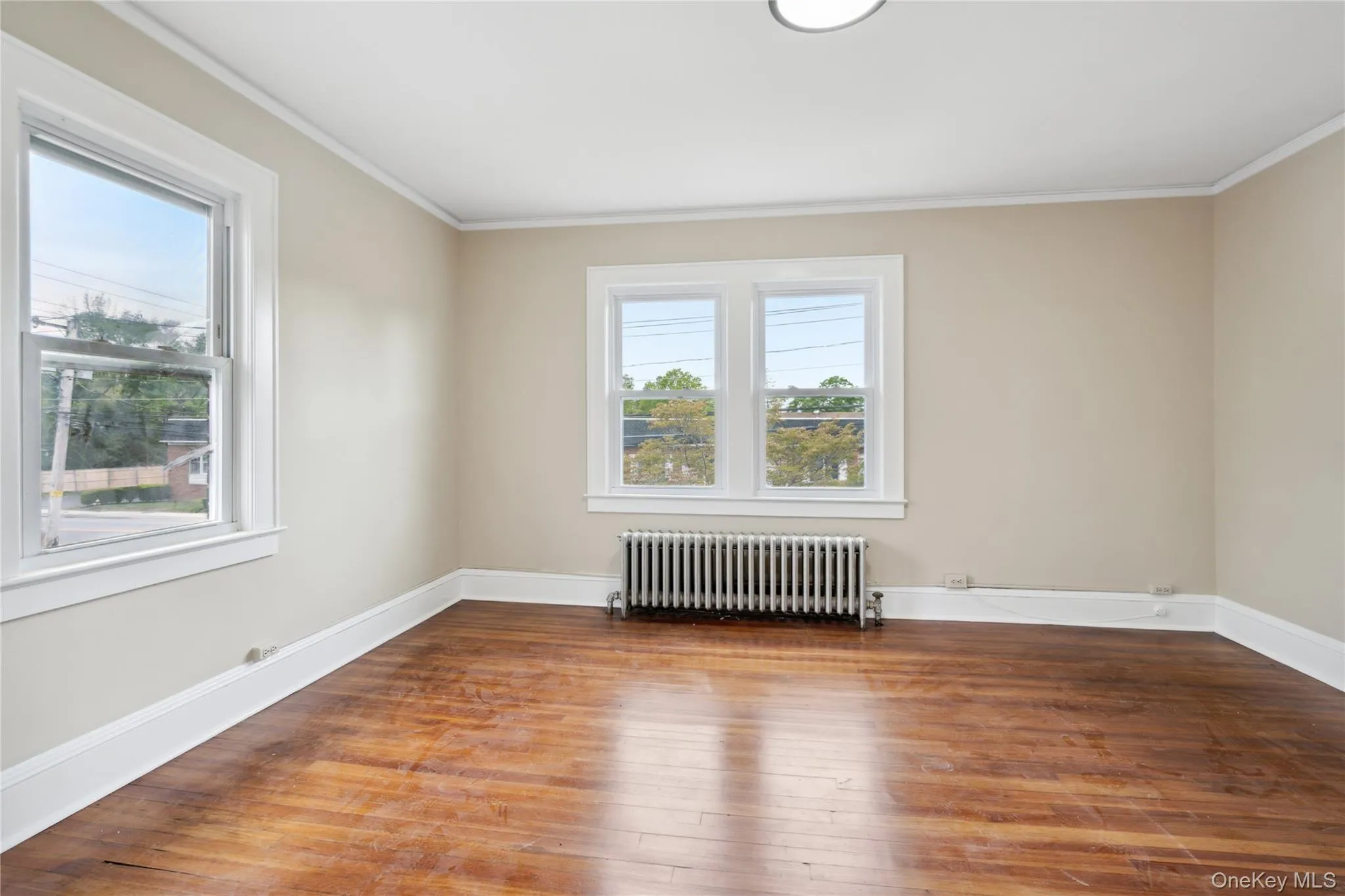 Spare room featuring radiator, ornamental molding, wood-type flooring, and healthy amount of natural light Spare room featuring radiator, ornamental molding, wood-type flooring, and healthy amount of natural light