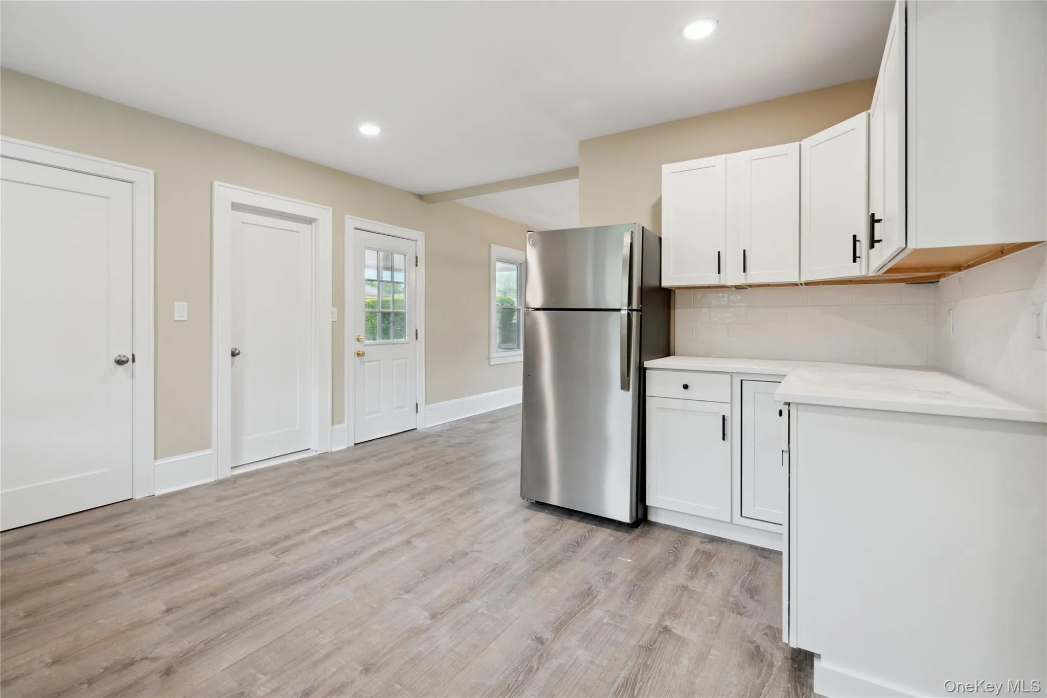 Kitchen featuring freestanding refrigerator, light countertops, white cabinets, light wood-type flooring, and backsplash Kitchen featuring freestanding refrigerator, light countertops, white cabinets, light wood-type flooring, and backsplash