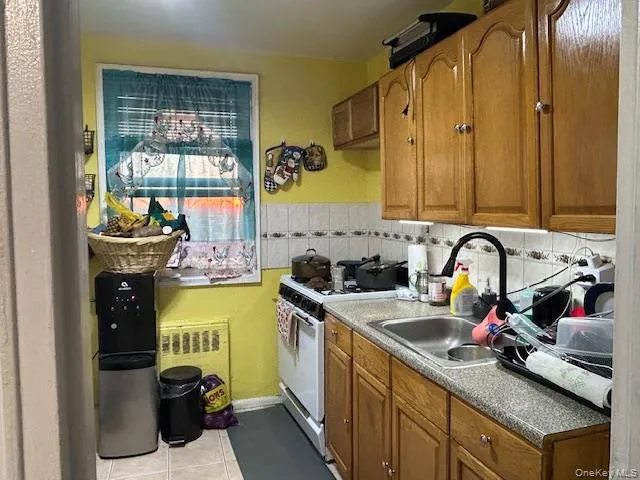 Kitchen with white range with gas stovetop, brown cabinets, light tile patterned flooring, and radiator Kitchen with white range with gas stovetop, brown cabinets, light tile patterned flooring, and radiator