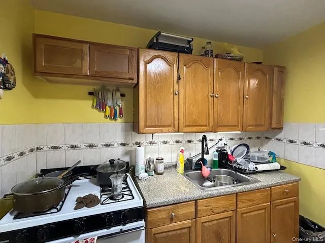 Kitchen with stove, light countertops, brown cabinetry, tile walls, and a wainscoted wall Kitchen with stove, light countertops, brown cabinetry, tile walls, and a wainscoted wall