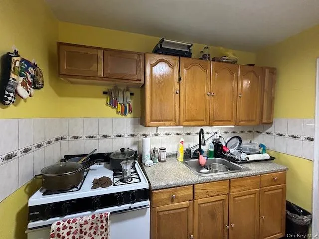 Kitchen with white range with gas stovetop, tile walls, light countertops, brown cabinetry, and wainscoting Kitchen with white range with gas stovetop, tile walls, light countertops, brown cabinetry, and wainscoting