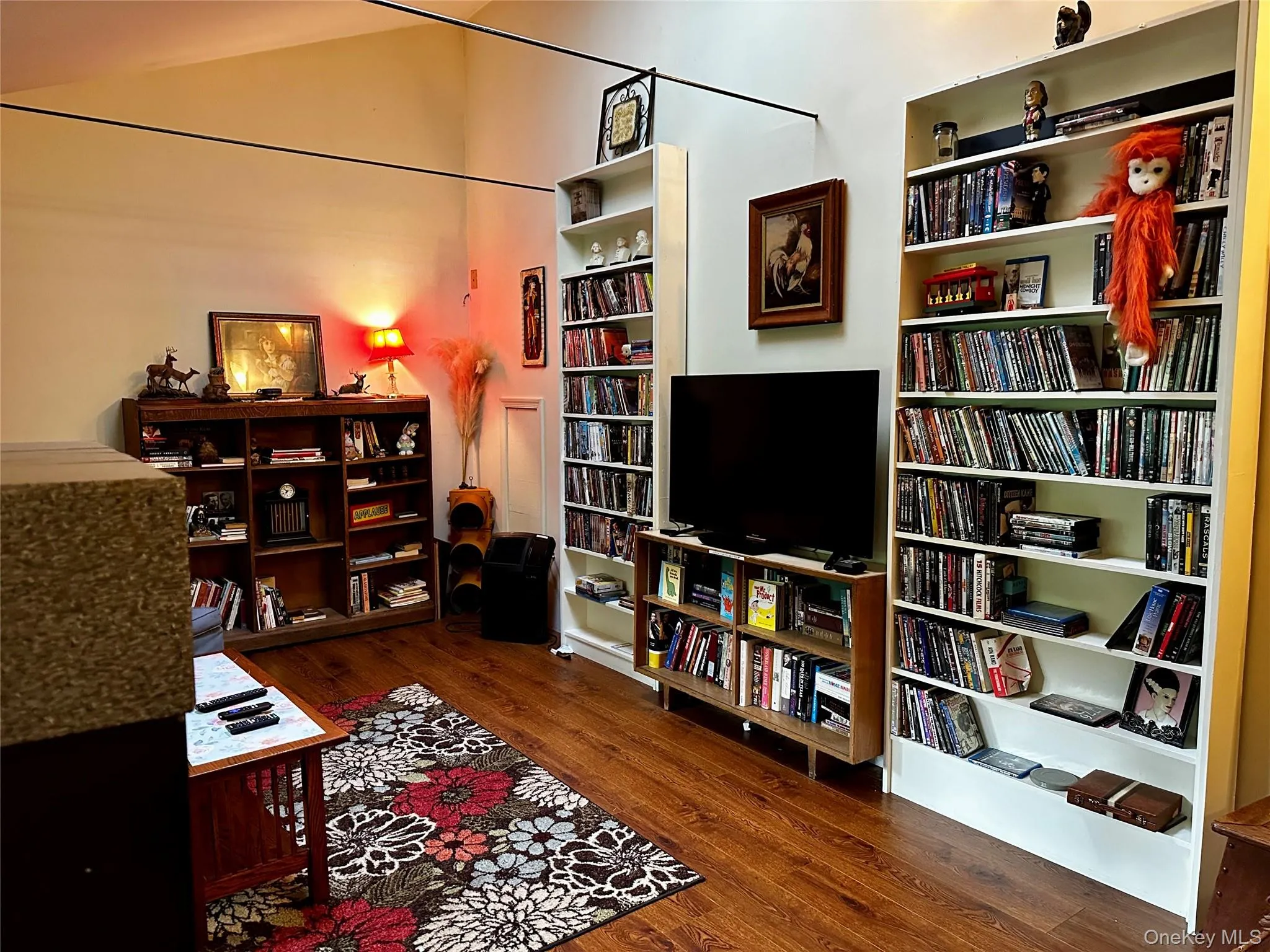 Sitting room featuring wood finished floors, wall of books, and vaulted ceiling Sitting room featuring wood finished floors, wall of books, and vaulted ceiling