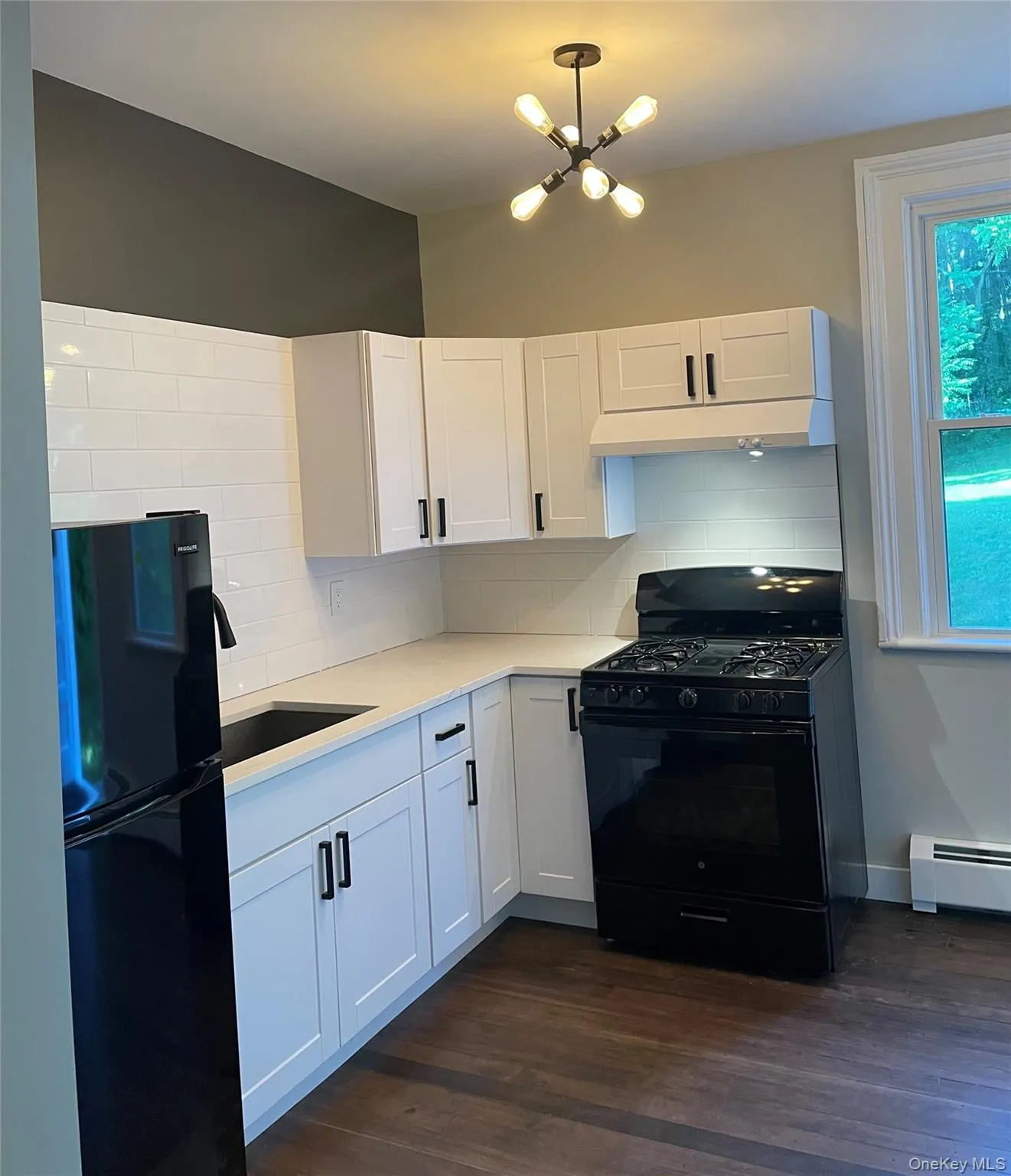 Kitchen with tasteful backsplash, black appliances, white cabinets, and dark wood-type flooring Kitchen with tasteful backsplash, black appliances, white cabinets, and dark wood-type flooring