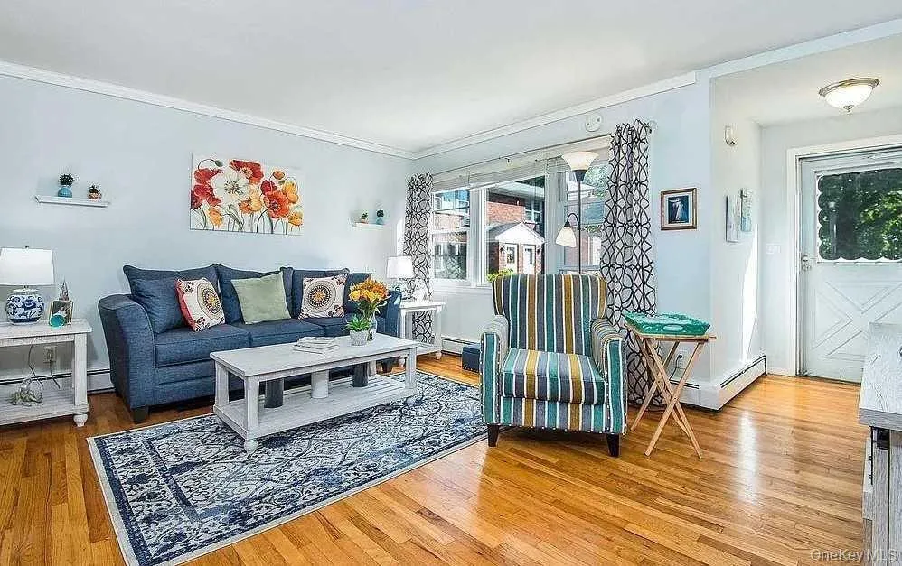 Living area featuring ornamental molding, light wood-type flooring, and a baseboard heating unit Living area featuring ornamental molding, light wood-type flooring, and a baseboard heating unit