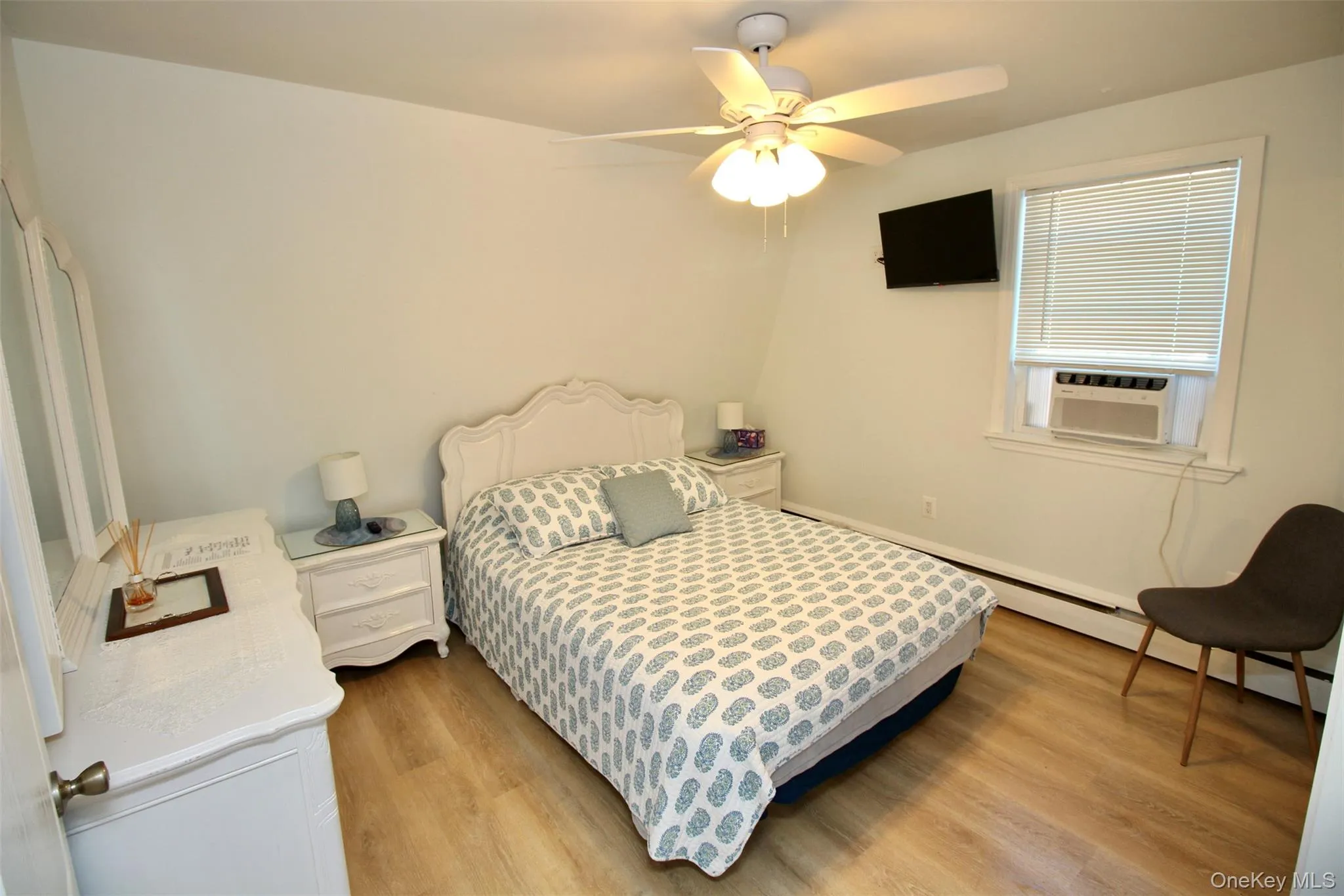 Bedroom featuring a baseboard radiator, light wood finished floors, ceiling fan, and cooling unit Bedroom featuring a baseboard radiator, light wood finished floors, ceiling fan, and cooling unit