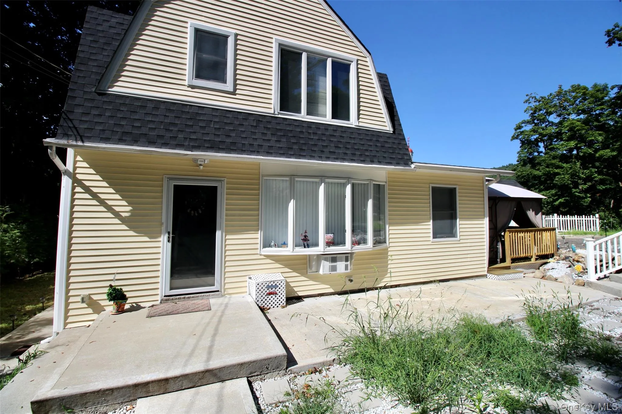 View of front facade with a gazebo, a gambrel roof, roof with shingles, and a patio View of front facade with a gazebo, a gambrel roof, roof with shingles, and a patio