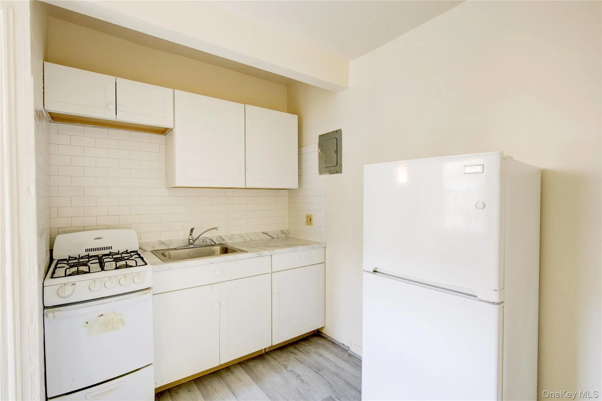 Kitchen with white appliances, decorative backsplash, light countertops, white cabinets, and light wood-type flooring Kitchen with white appliances, decorative backsplash, light countertops, white cabinets, and light wood-type flooring