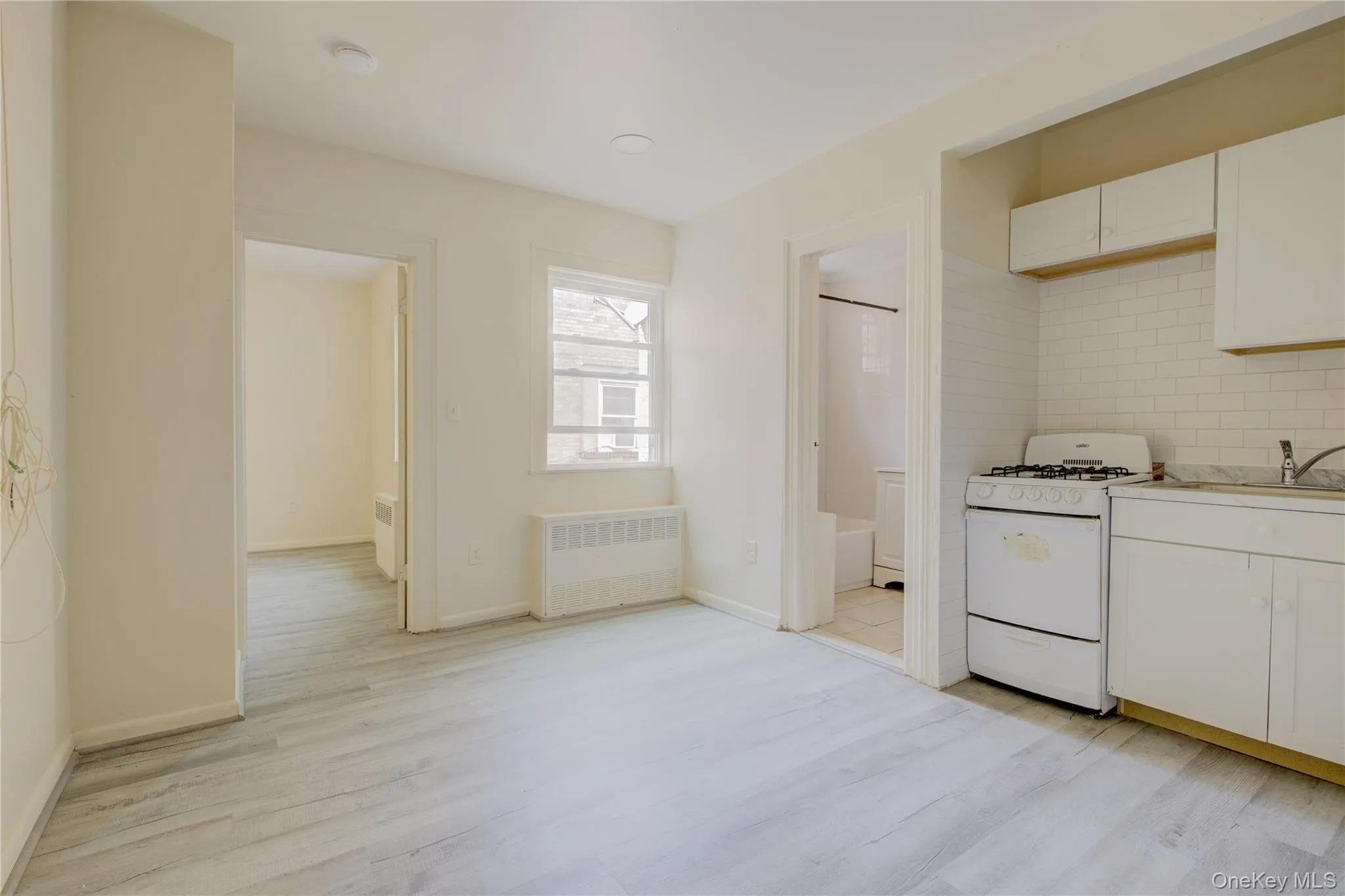 Kitchen with white range with gas cooktop, tasteful backsplash, radiator, and light wood-style flooring Kitchen with white range with gas cooktop, tasteful backsplash, radiator, and light wood-style flooring