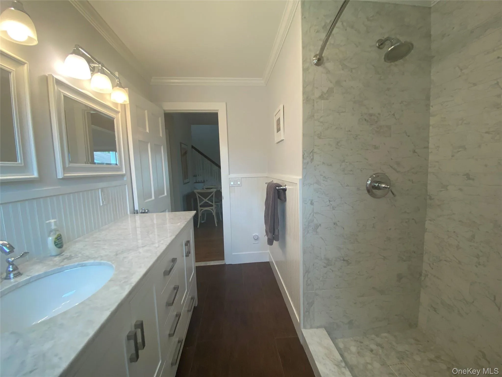 Bathroom with ornamental molding, tiled shower, wood finished floors, vanity, and wainscoting Bathroom with ornamental molding, tiled shower, wood finished floors, vanity, and wainscoting