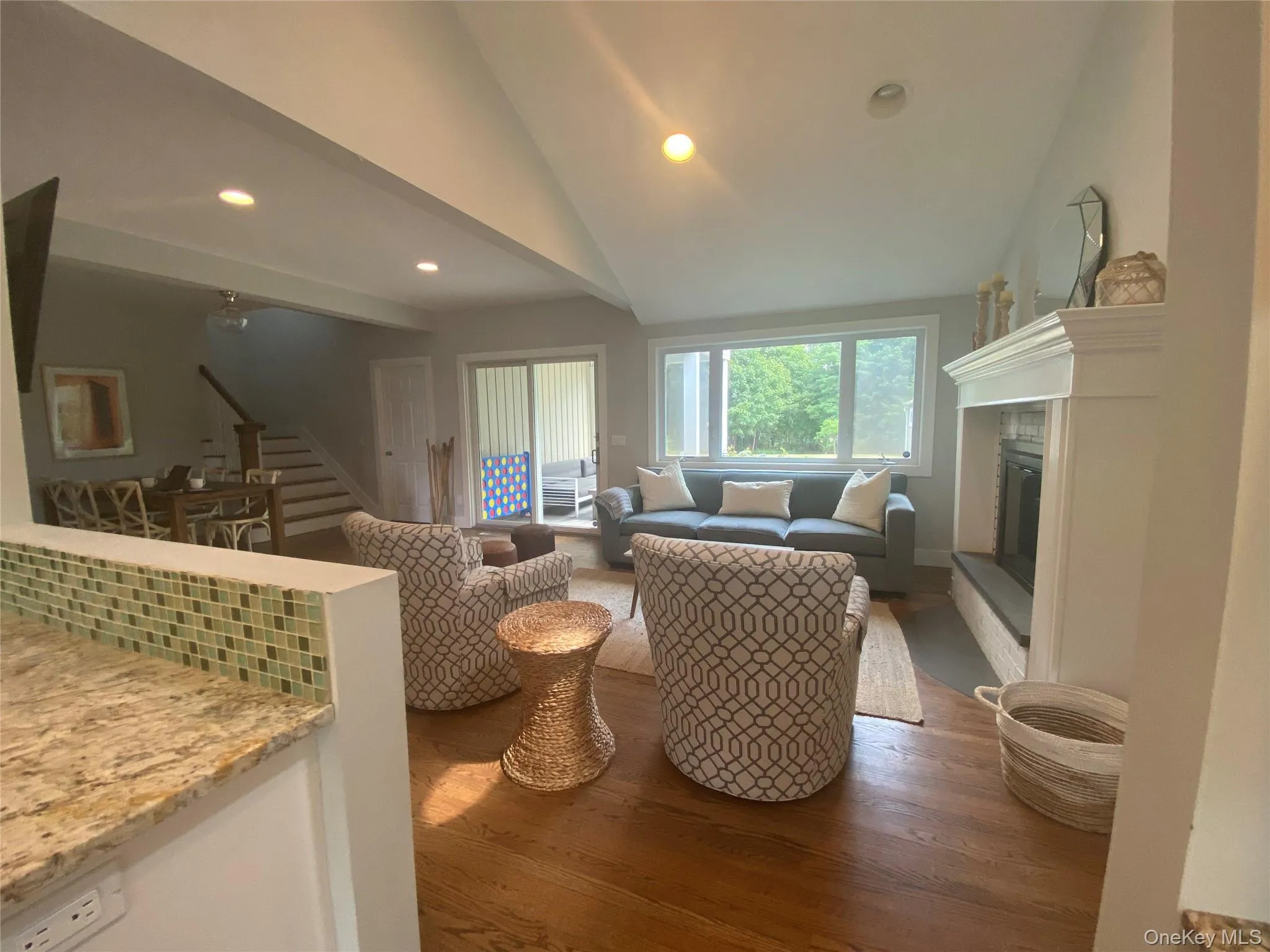 Living room featuring vaulted ceiling, a glass covered fireplace, recessed lighting, wood finished floors, and stairway Living room featuring vaulted ceiling, a glass covered fireplace, recessed lighting, wood finished floors, and stairway