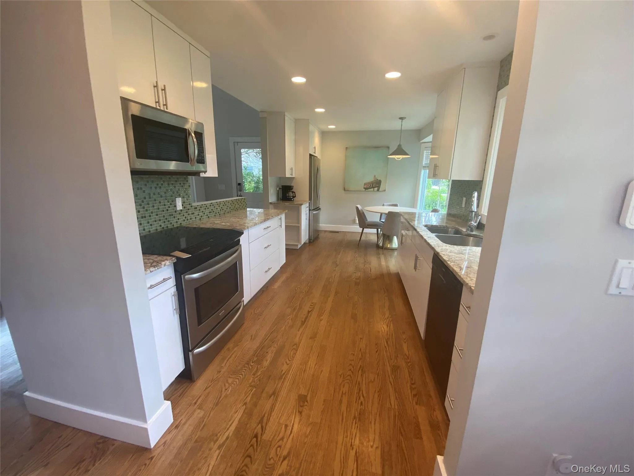 Kitchen with stainless steel appliances, decorative backsplash, white cabinetry, wood finished floors, and light stone counters Kitchen with stainless steel appliances, decorative backsplash, white cabinetry, wood finished floors, and light stone counters