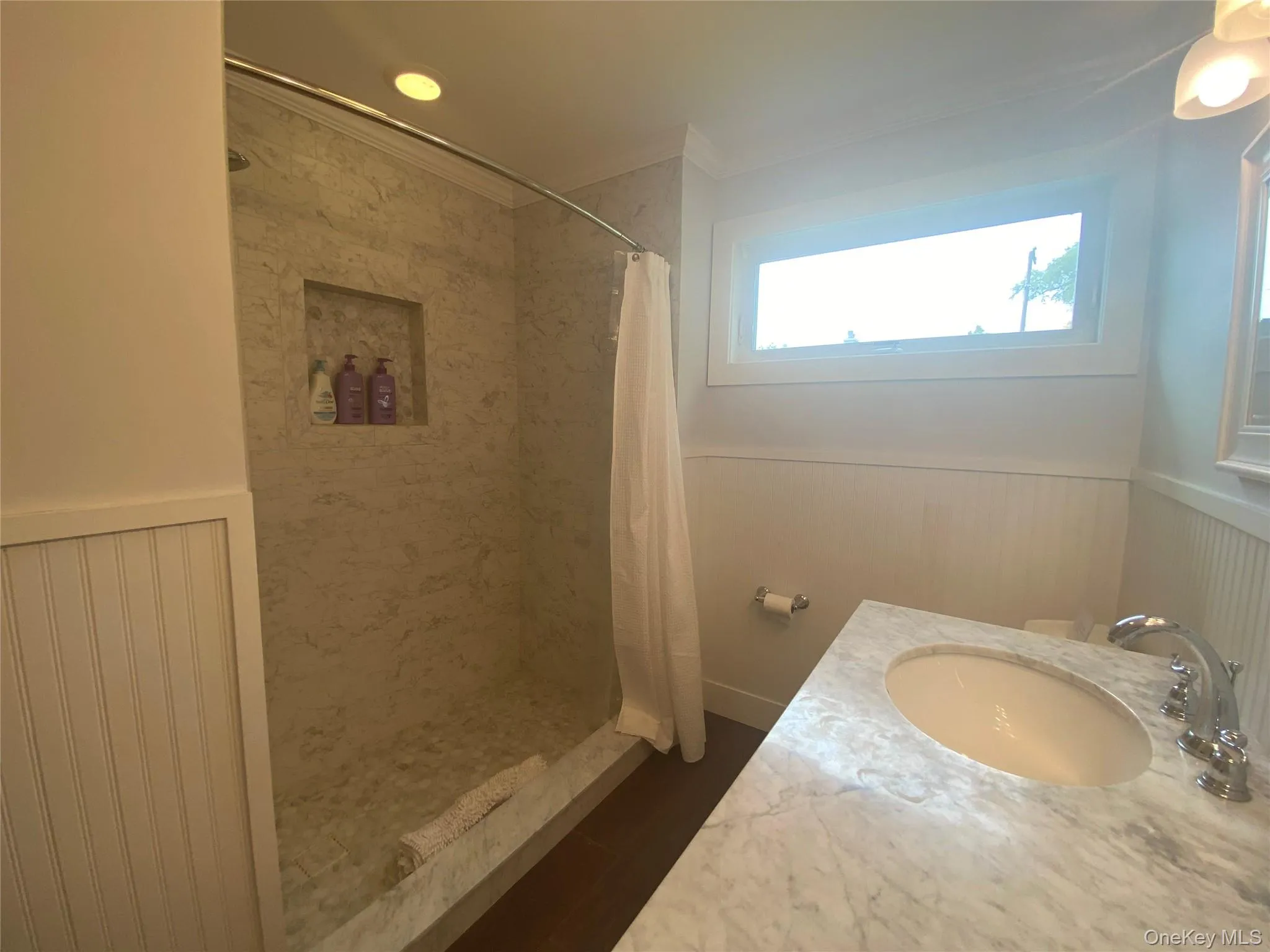 Full bath with wainscoting, a tile shower, ornamental molding, a decorative wall, and wood finished floors Full bath with wainscoting, a tile shower, ornamental molding, a decorative wall, and wood finished floors