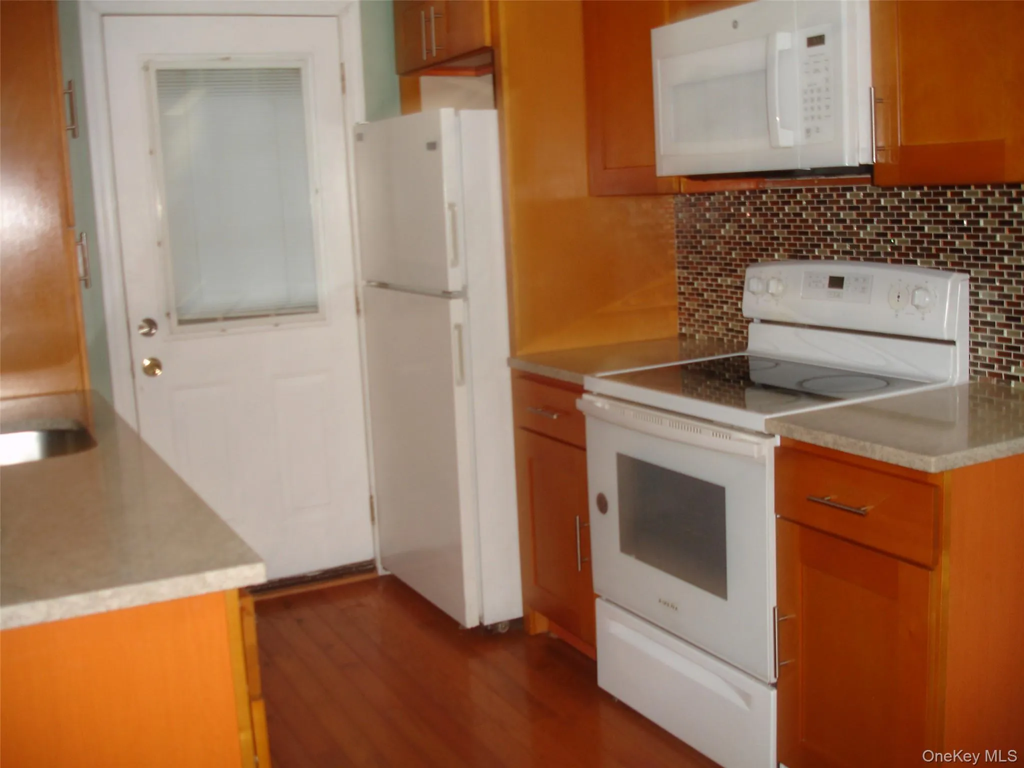 Kitchen with white appliances, dark wood-style flooring, tasteful backsplash, light countertops, and brown cabinets Kitchen with white appliances, dark wood-style flooring, tasteful backsplash, light countertops, and brown cabinets