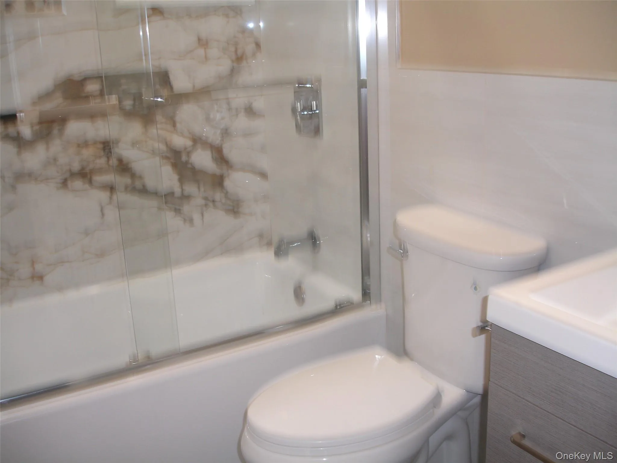 Bathroom featuring vanity, shower / bath combination with glass door, and tile walls Bathroom featuring vanity, shower / bath combination with glass door, and tile walls