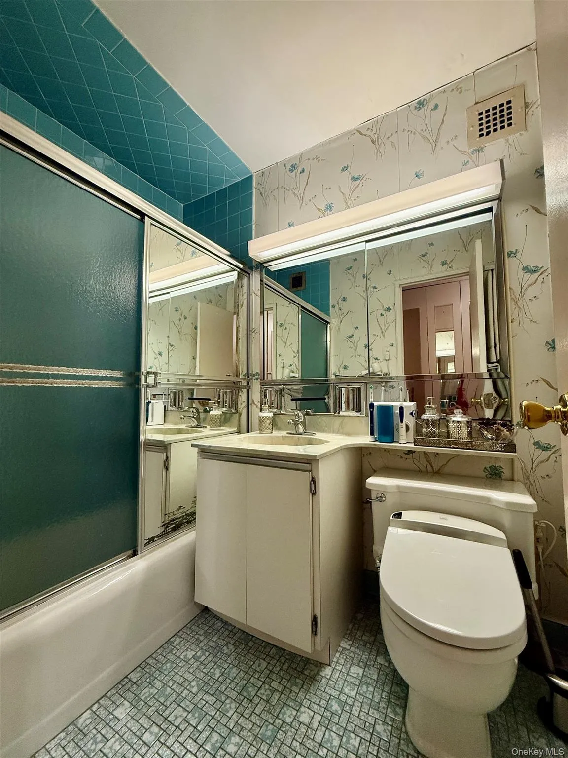 Bathroom featuring wallpapered walls, bath / shower combo with glass door, and vanity Bathroom featuring wallpapered walls, bath / shower combo with glass door, and vanity
