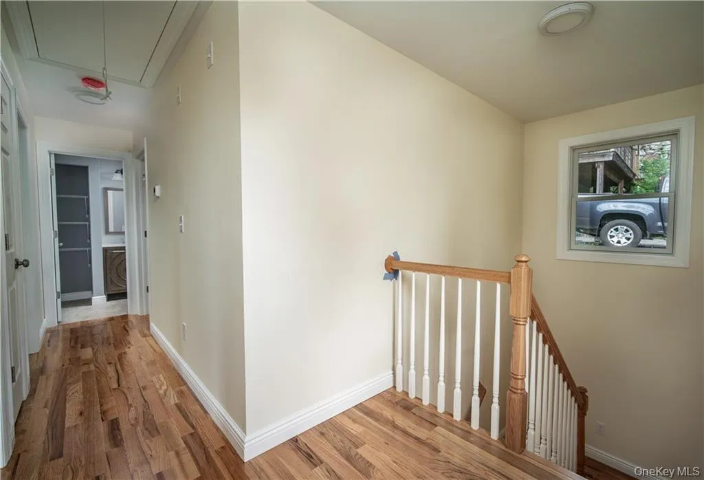 Hall with attic access, light wood finished floors, and an upstairs landing Hall with attic access, light wood finished floors, and an upstairs landing