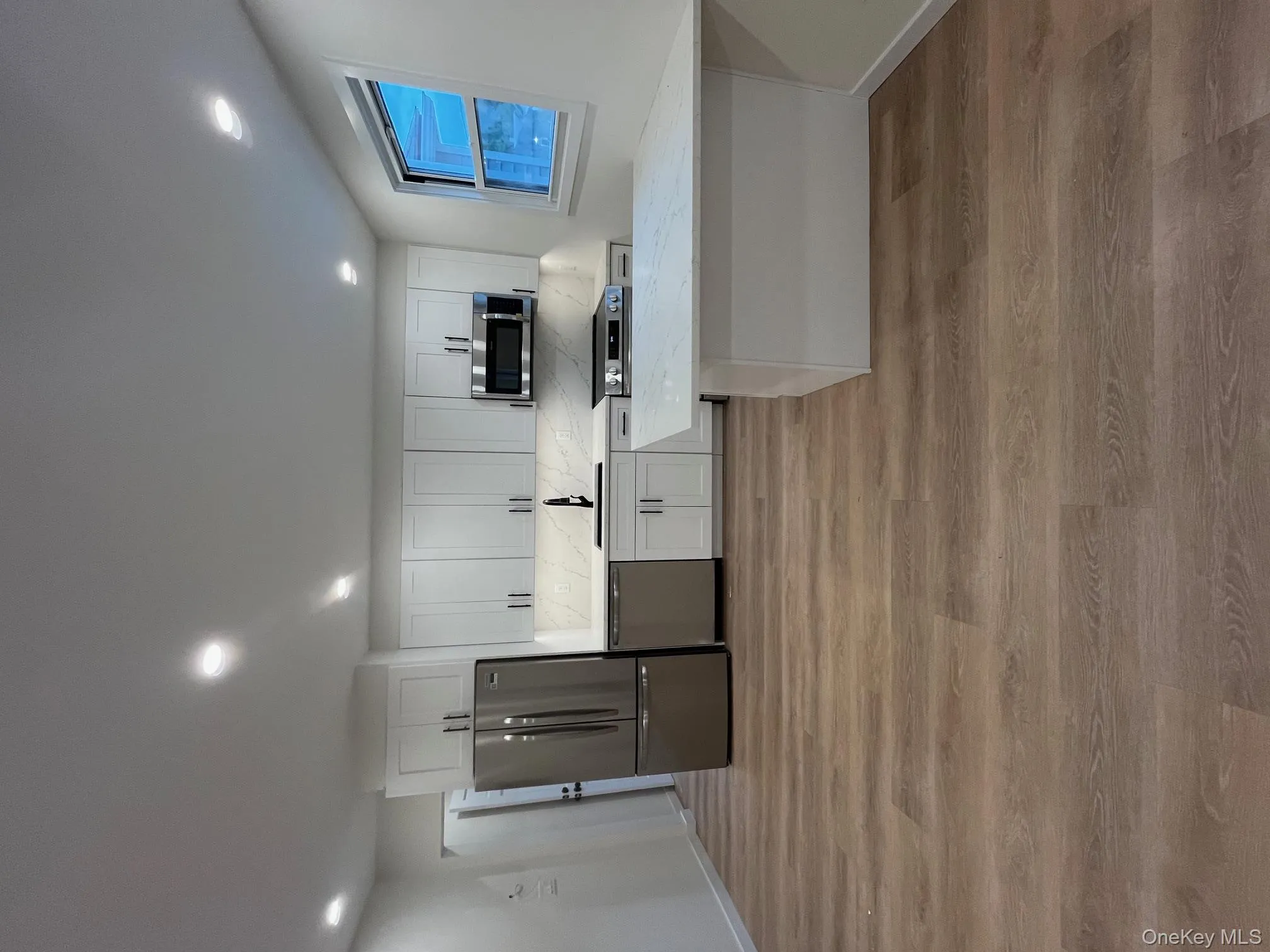 Kitchen with white cabinetry, a peninsula, fridge, light wood-type flooring, and light stone counters Kitchen with white cabinetry, a peninsula, fridge, light wood-type flooring, and light stone counters