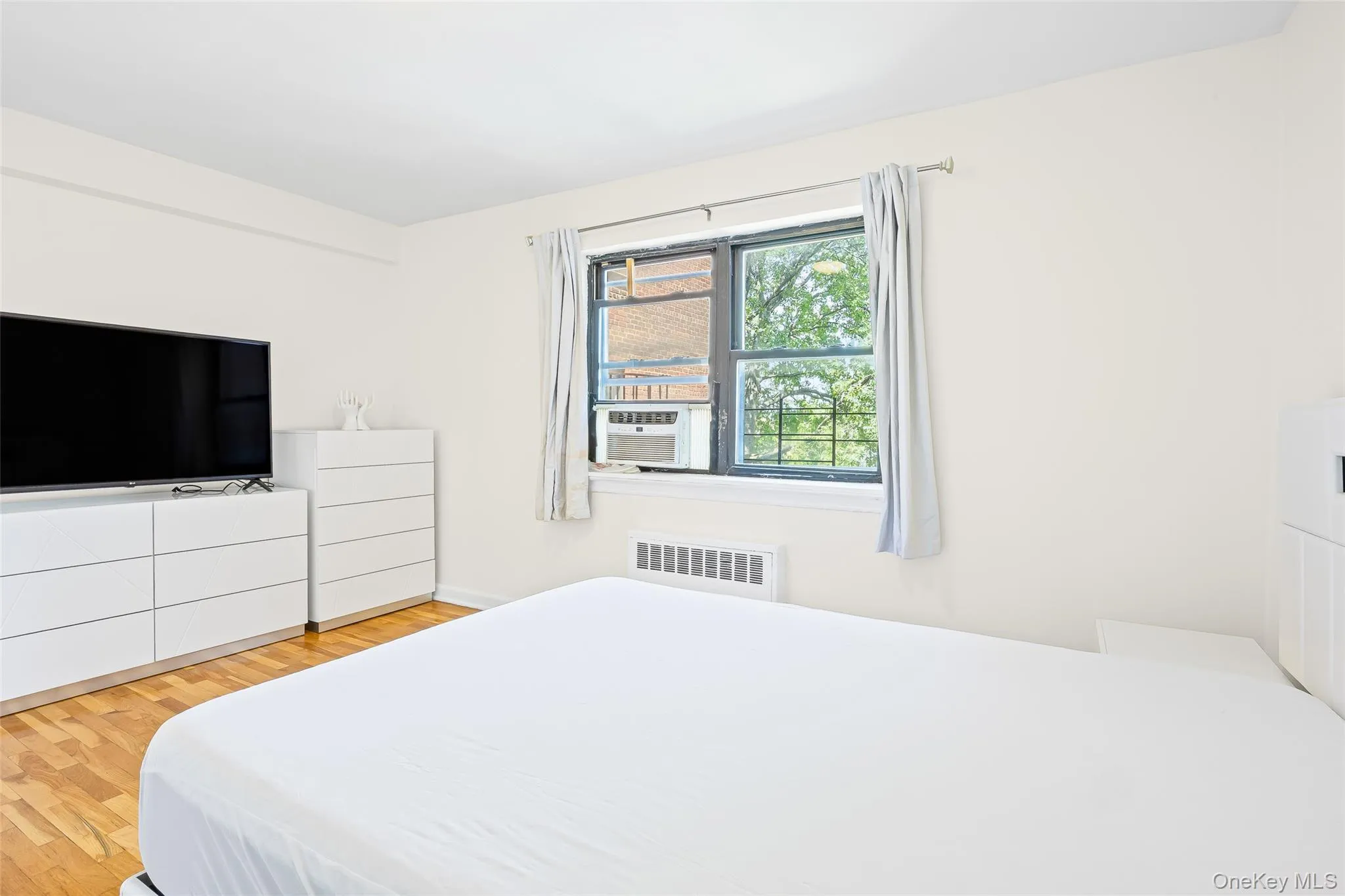 Bedroom featuring light wood-style flooring, radiator heating unit, and cooling unit Bedroom featuring light wood-style flooring, radiator heating unit, and cooling unit