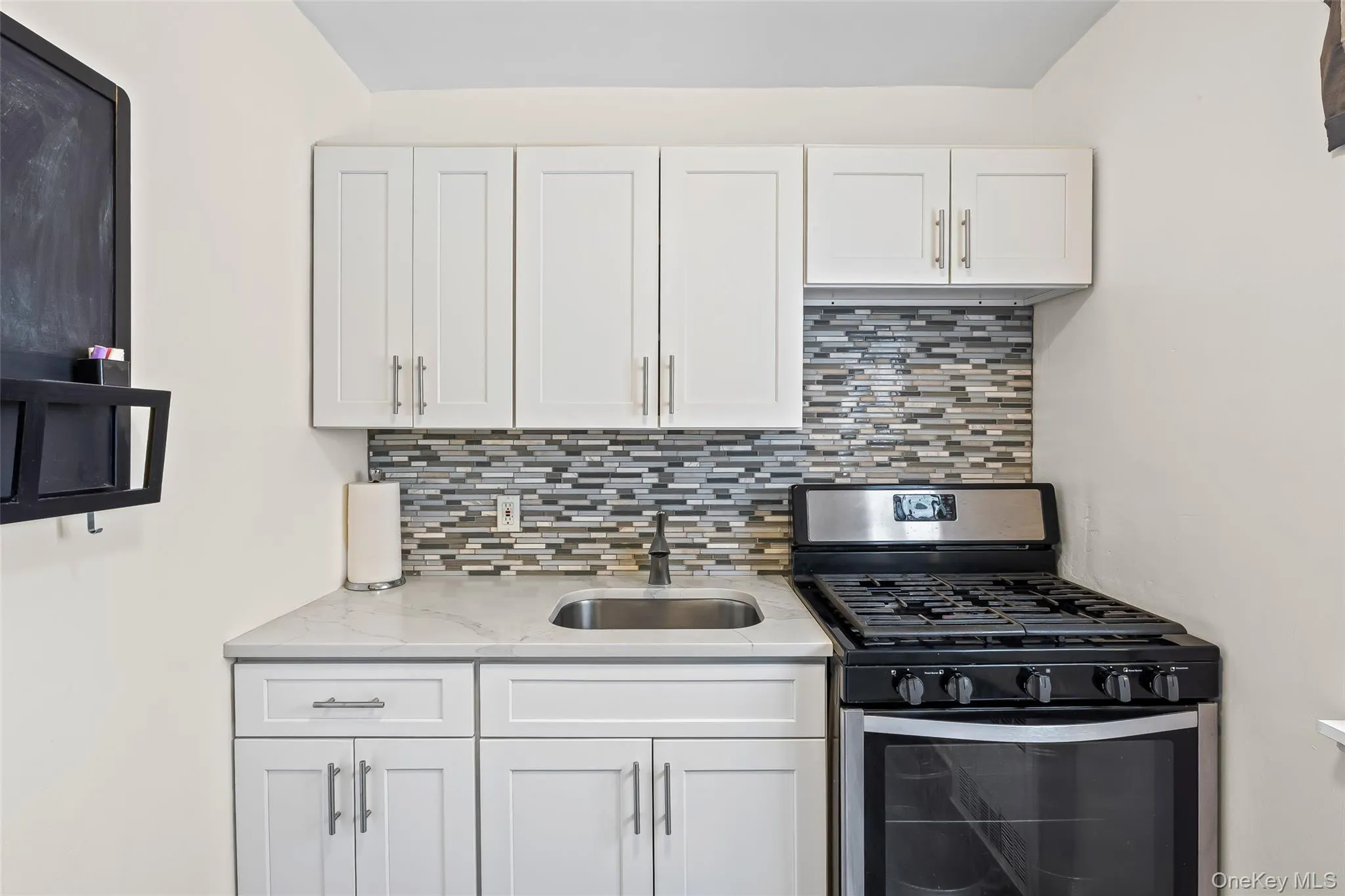 Kitchen with tasteful backsplash, gas stove, white cabinetry, and light stone countertops Kitchen with tasteful backsplash, gas stove, white cabinetry, and light stone countertops