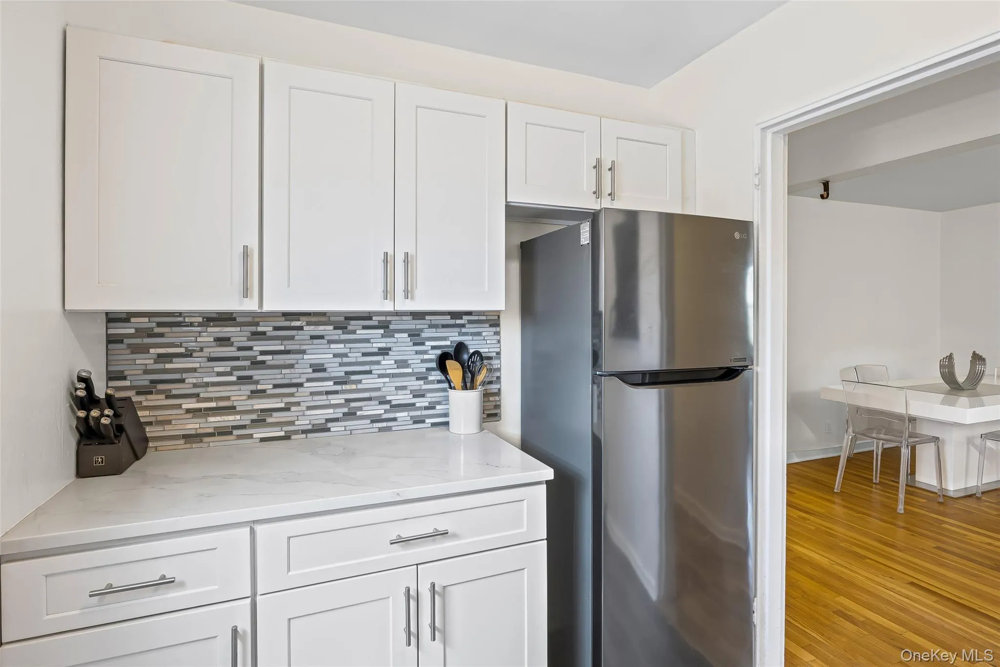Kitchen with freestanding refrigerator, backsplash, white cabinetry, light stone counters, and light wood-style flooring Kitchen with freestanding refrigerator, backsplash, white cabinetry, light stone counters, and light wood-style flooring