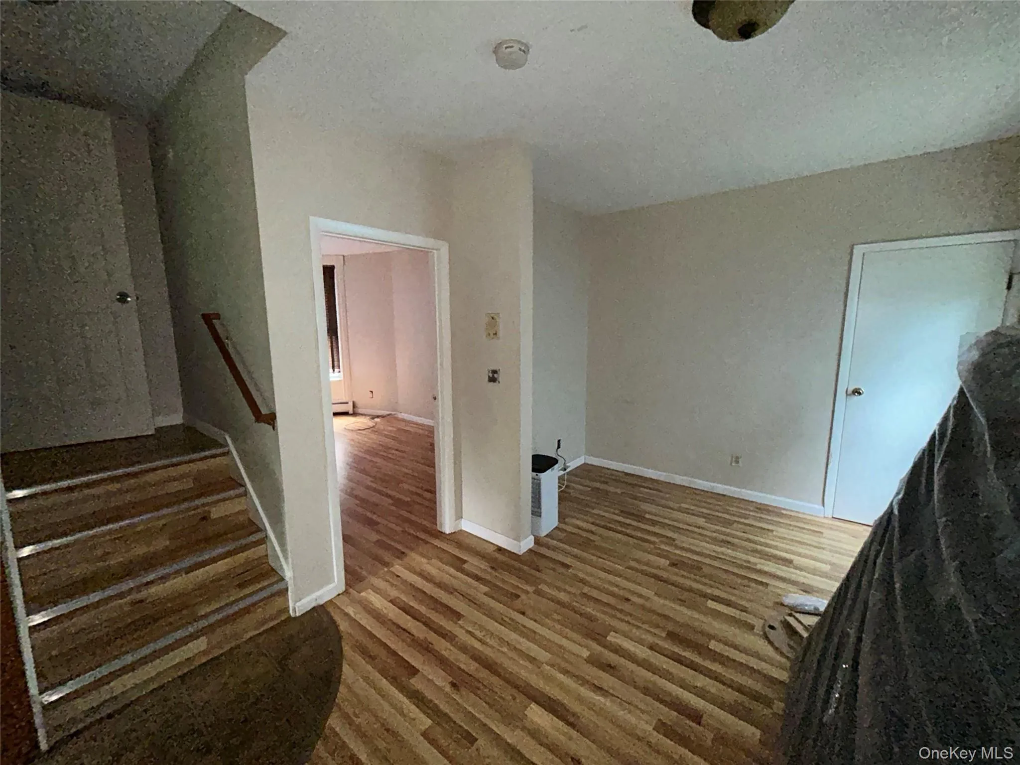Unfurnished living room featuring wood finished floors, a textured ceiling, and stairs Unfurnished living room featuring wood finished floors, a textured ceiling, and stairs