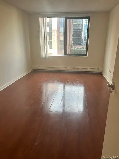 Spare room with dark wood finished floors, a textured ceiling, and a baseboard heating unit Spare room with dark wood finished floors, a textured ceiling, and a baseboard heating unit