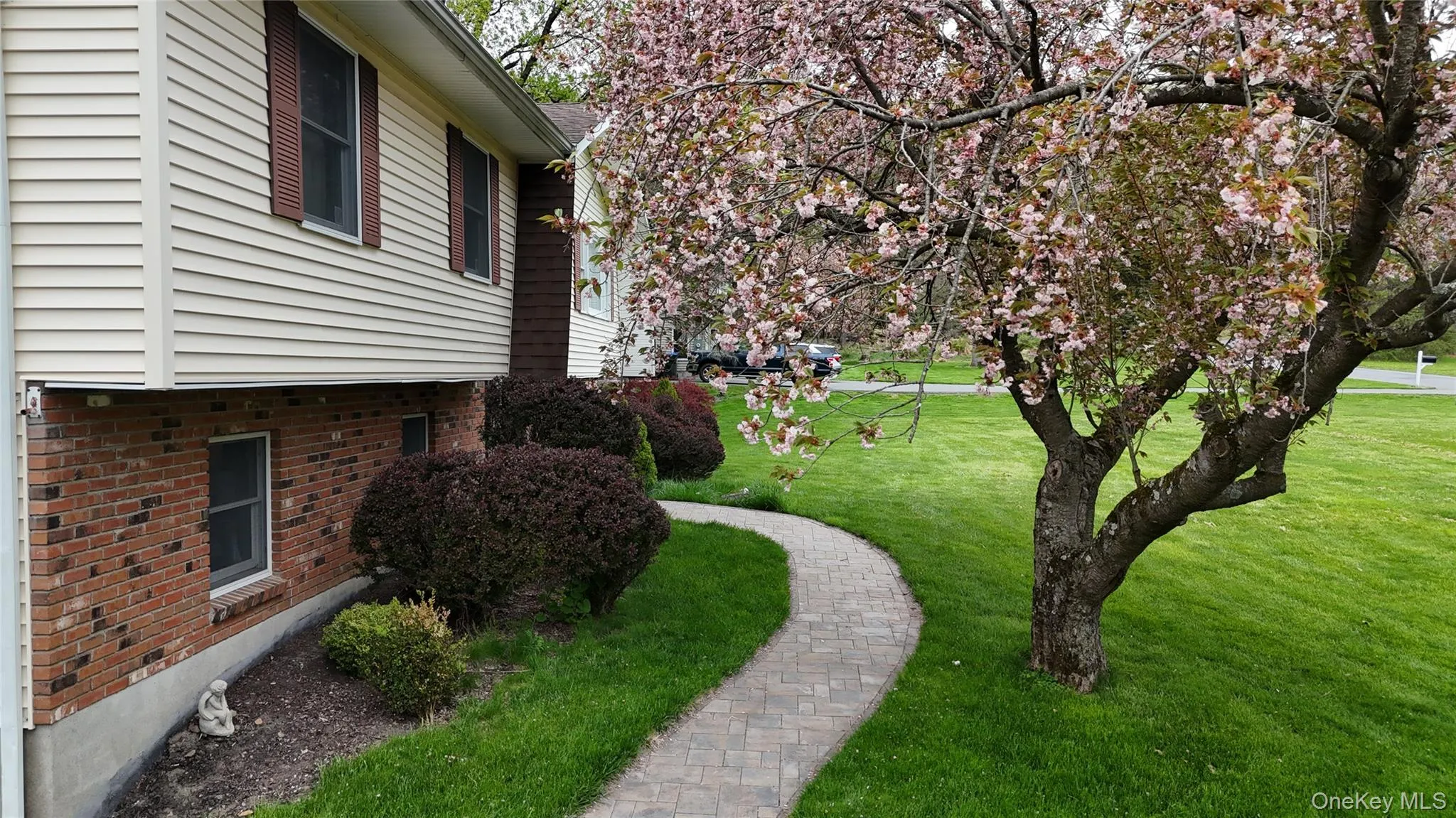 Charming paver stone winding pathway from the driveway to the front door flanked by a flowering tree with delicate pink blossoms and flower beds Charming paver stone winding pathway from the driveway to the front door flanked by a flowering tree with delicate pink blossoms and flower beds