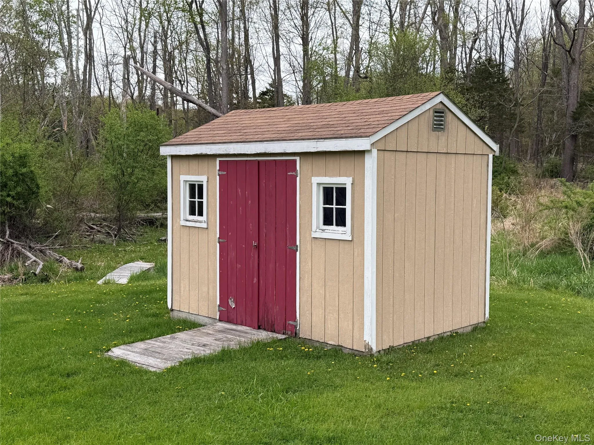 Freestanding storage shed featuring tan siding with white trim and a brown shingle roof Freestanding storage shed featuring tan siding with white trim and a brown shingle roof