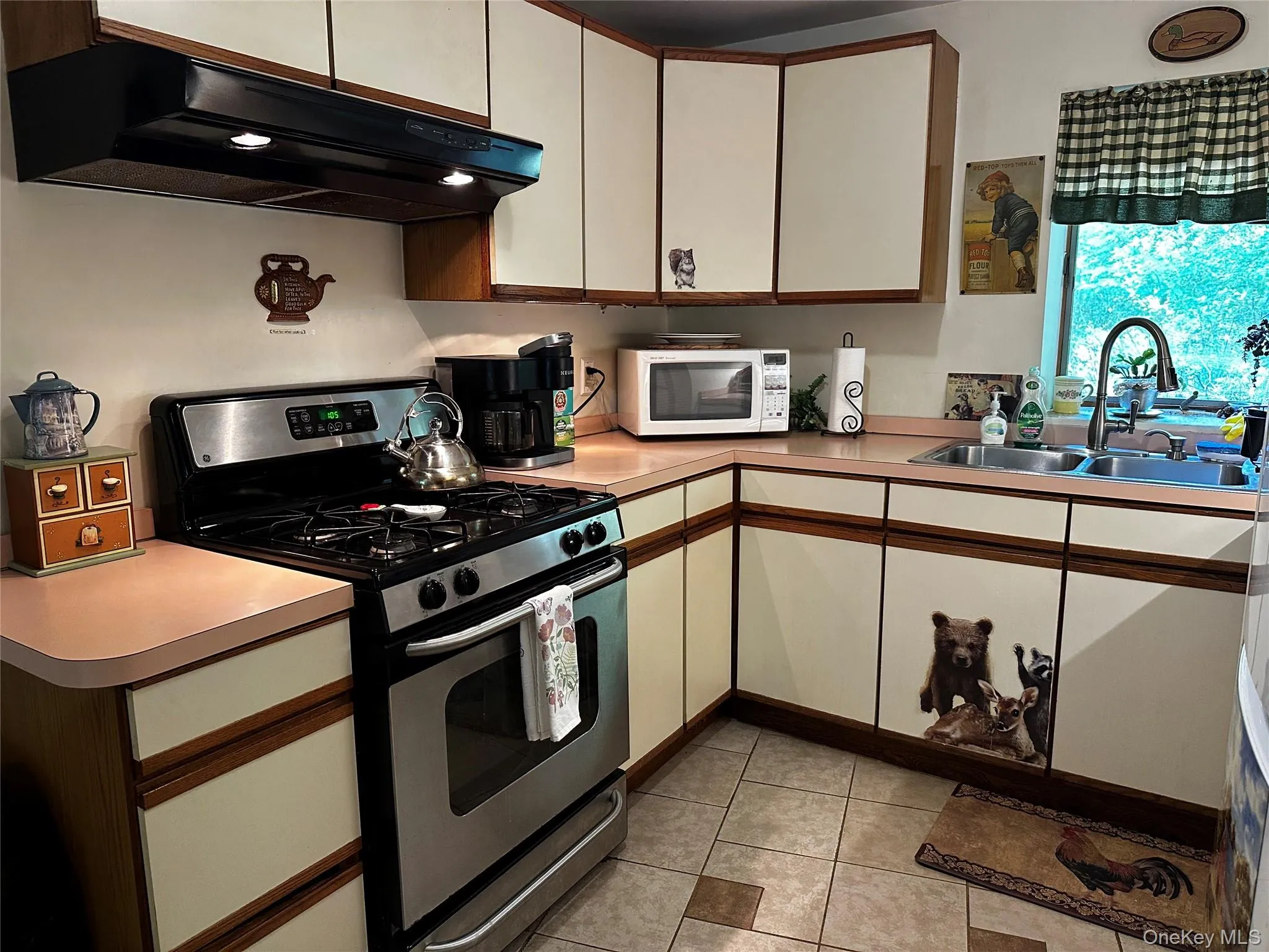 Kitchen with gas range, under cabinet range hood, white microwave, light tile patterned floors, and light countertops Kitchen with gas range, under cabinet range hood, white microwave, light tile patterned floors, and light countertops