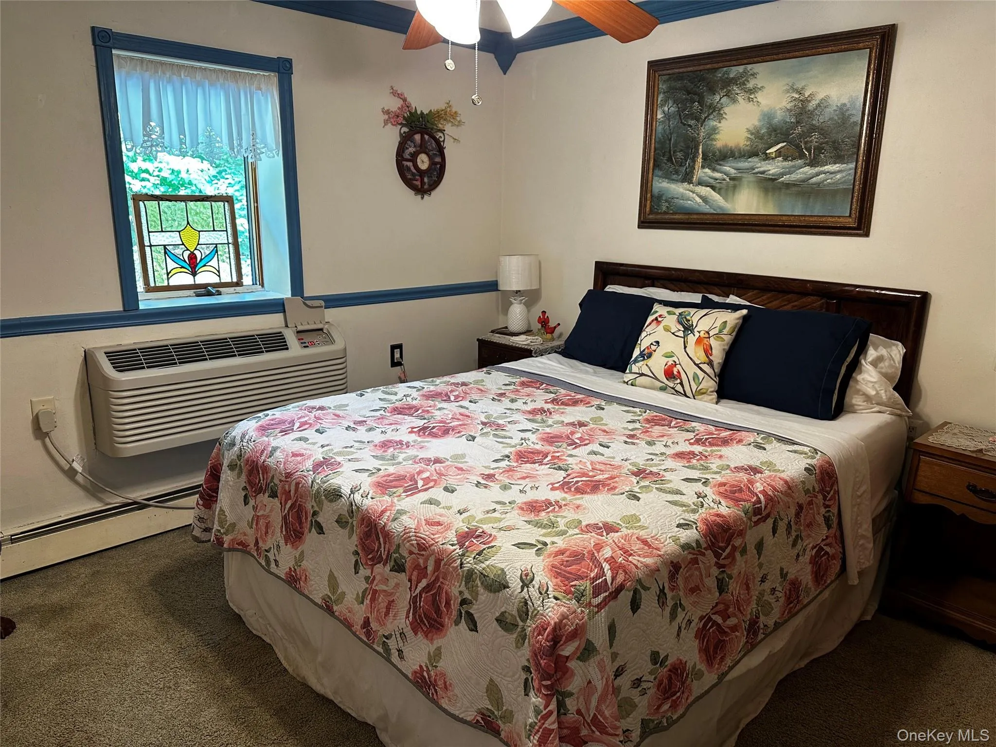 Carpeted bedroom featuring baseboard heating, a ceiling fan, ornamental molding, and a wall mounted air conditioner Carpeted bedroom featuring baseboard heating, a ceiling fan, ornamental molding, and a wall mounted air conditioner