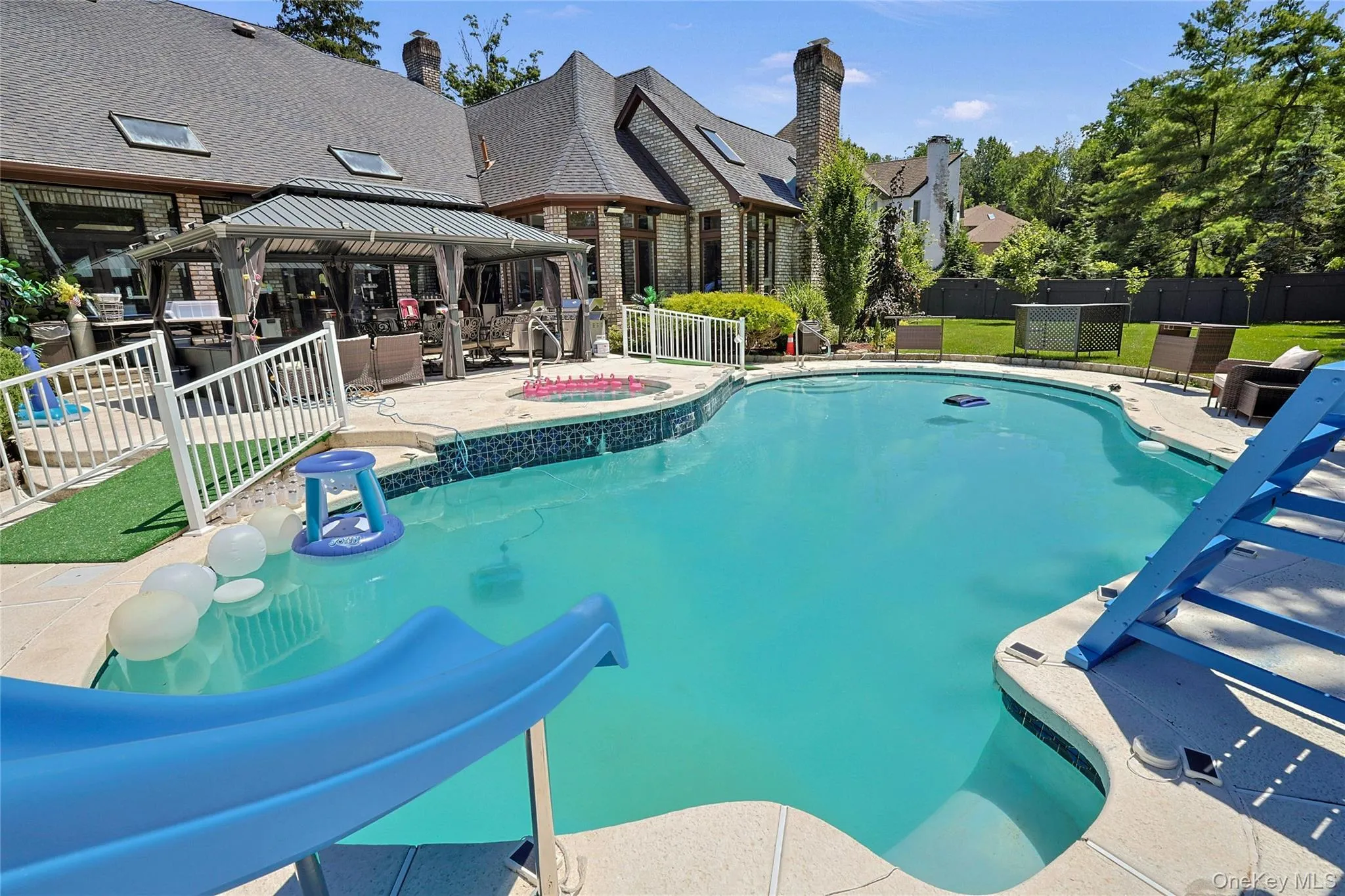 View of pool with a gazebo, a fenced backyard, a patio, a water slide, and a pool with connected hot tub View of pool with a gazebo, a fenced backyard, a patio, a water slide, and a pool with connected hot tub