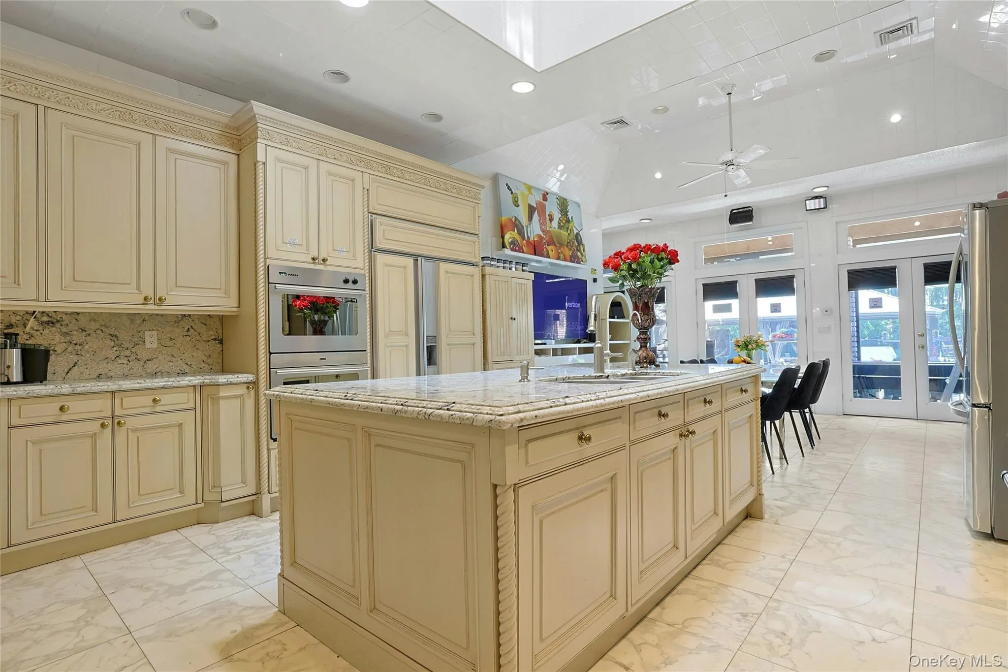 Kitchen featuring cream cabinetry, light marble finish flooring, an island with sink, light stone counters Kitchen featuring cream cabinetry, light marble finish flooring, an island with sink, light stone counters