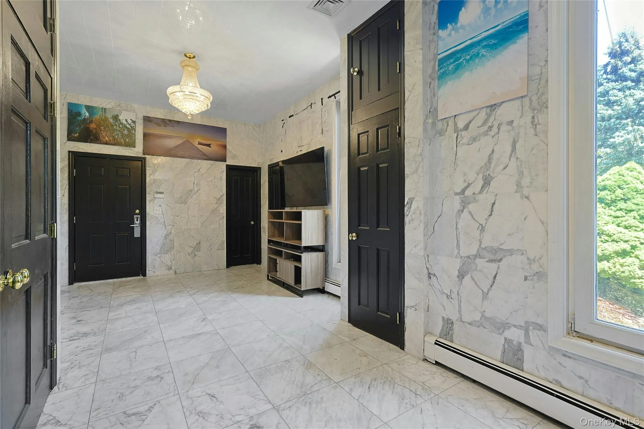 Entryway featuring baseboard heating, light marble finish floors, tile walls, and a chandelier Entryway featuring baseboard heating, light marble finish floors, tile walls, and a chandelier