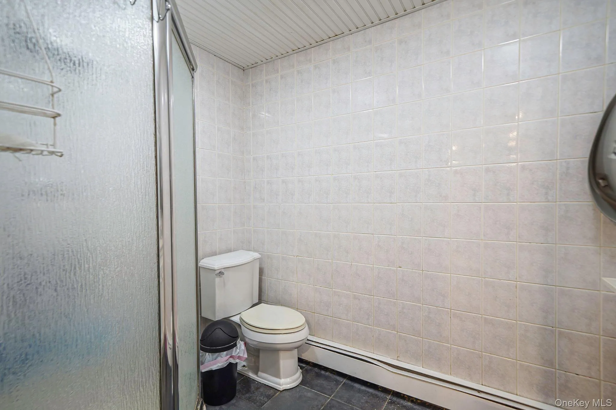 Full bath featuring a baseboard radiator, tile patterned flooring, a stall shower, and tile walls Full bath featuring a baseboard radiator, tile patterned flooring, a stall shower, and tile walls
