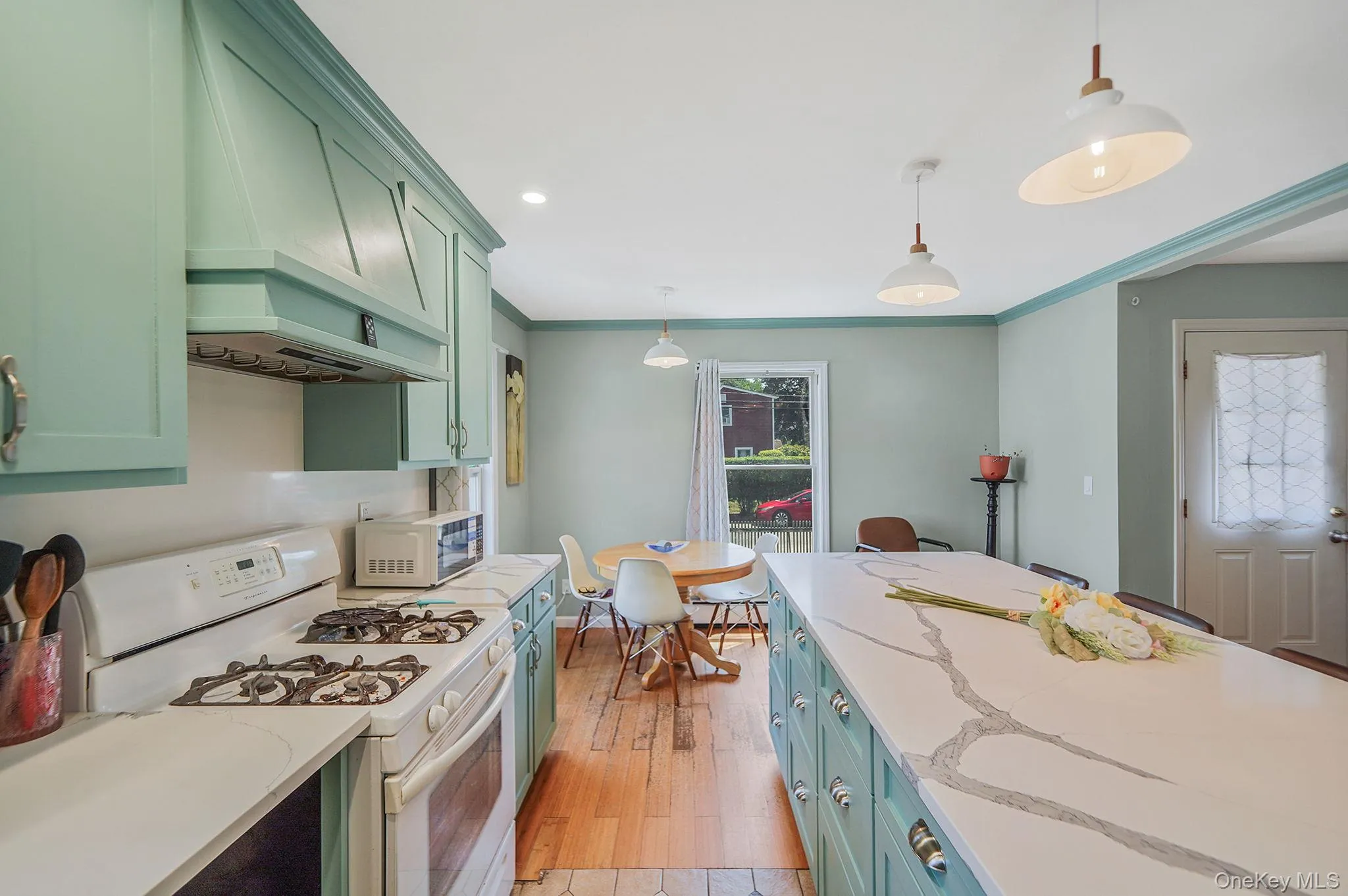 Kitchen with green cabinetry, white appliances, premium range hood, light wood-style flooring, and hanging light fixtures Kitchen with green cabinetry, white appliances, premium range hood, light wood-style flooring, and hanging light fixtures