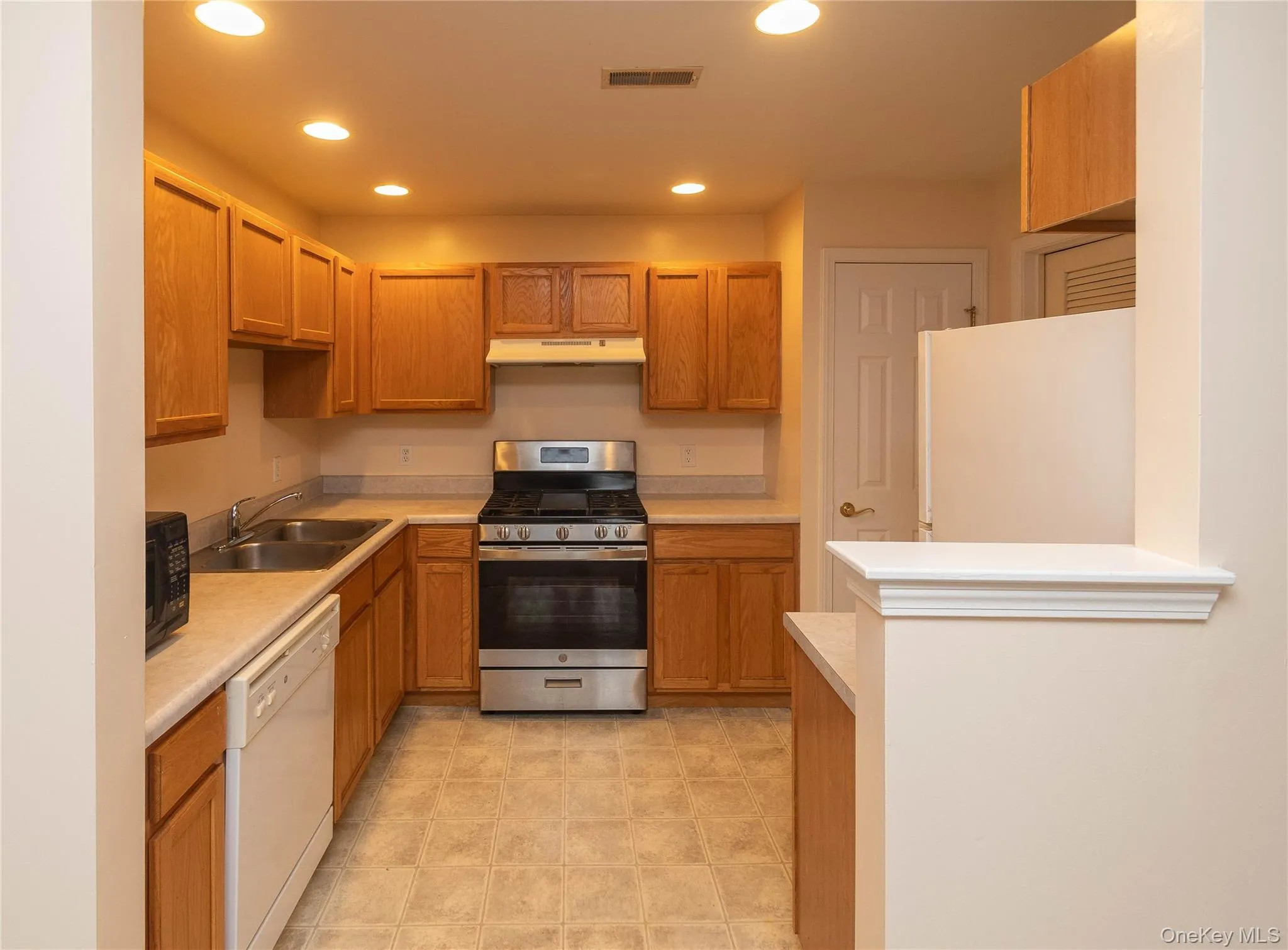 Kitchen with white appliances, recessed lighting, light countertops, under cabinet range hood, and brown cabinets Kitchen with white appliances, recessed lighting, light countertops, under cabinet range hood, and brown cabinets