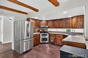 Kitchen with appliances with stainless steel finishes, beamed ceiling, dark wood-style floors, light countertops, and brown cabinets Kitchen with appliances with stainless steel finishes, beamed ceiling, dark wood-style floors, light countertops, and brown cabinets