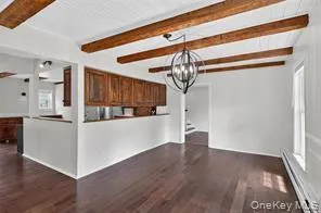 Unfurnished living room with beam ceiling, a chandelier, dark wood-type flooring, and a baseboard radiator Unfurnished living room with beam ceiling, a chandelier, dark wood-type flooring, and a baseboard radiator